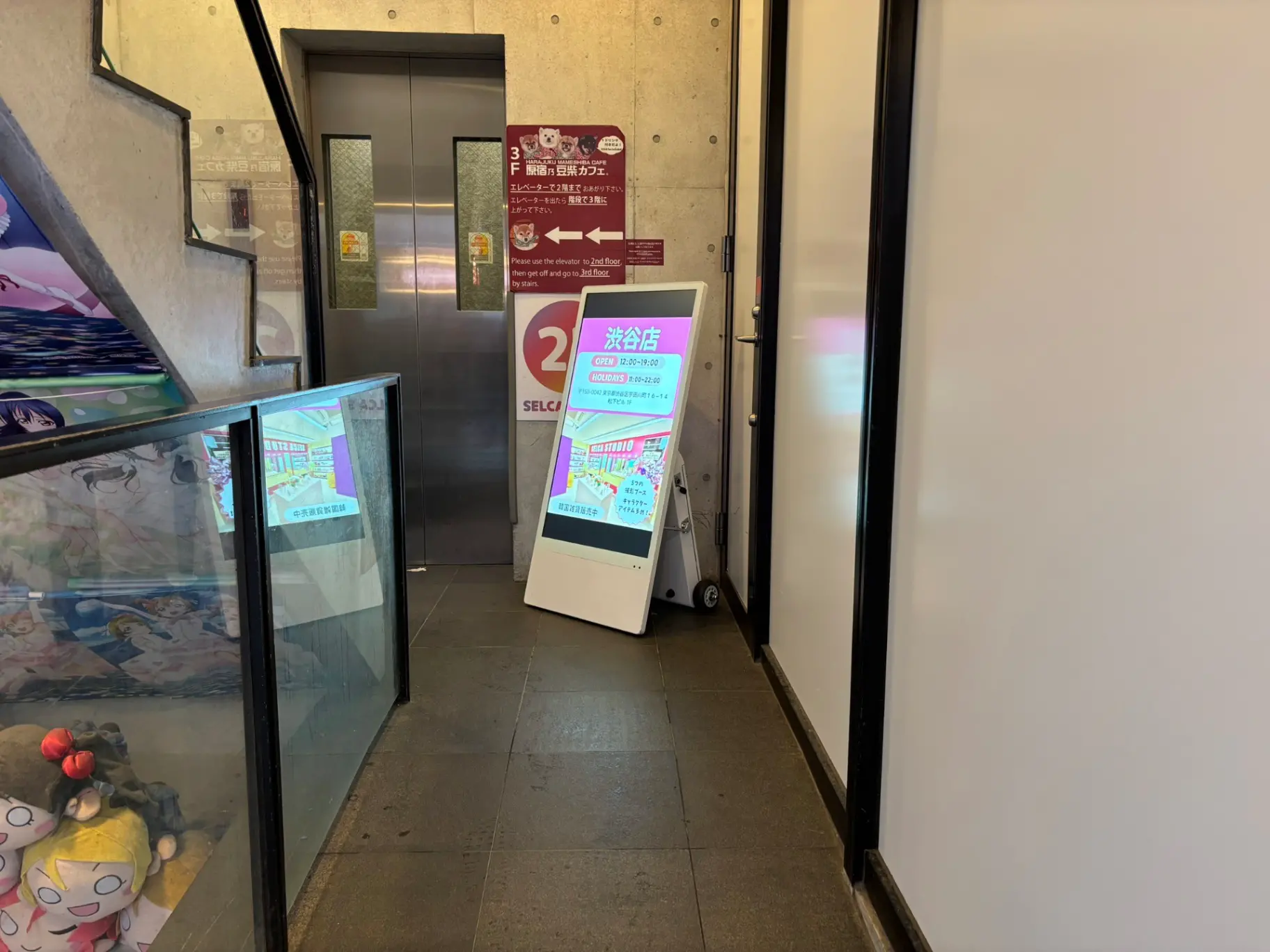 - 渋谷の店舗に向かうエレベーター前の通路、デジタルサイネージとアニメキャラクターが描かれたグラフィックが見える商業スペース