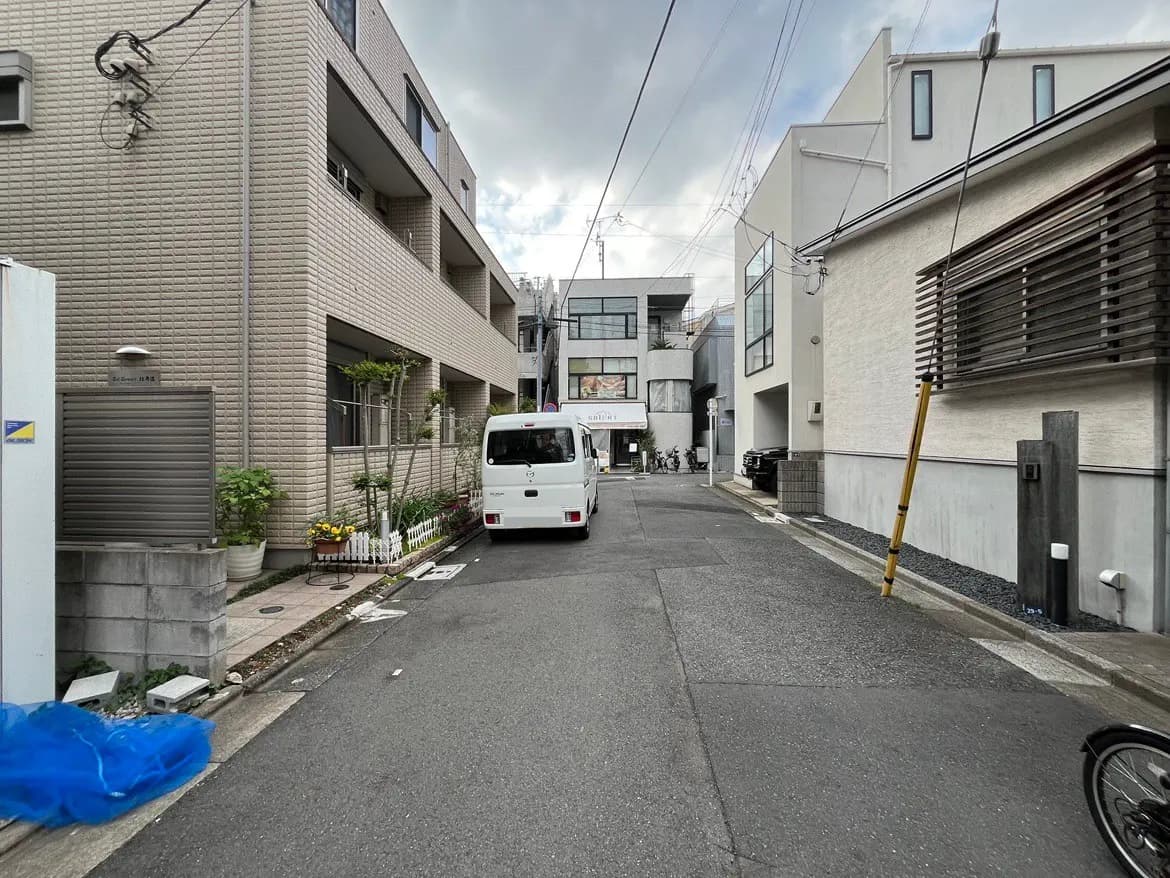 - 都市の住宅エリアの通り、住宅、白いバン、緑の植栽と青いシートが見える風景