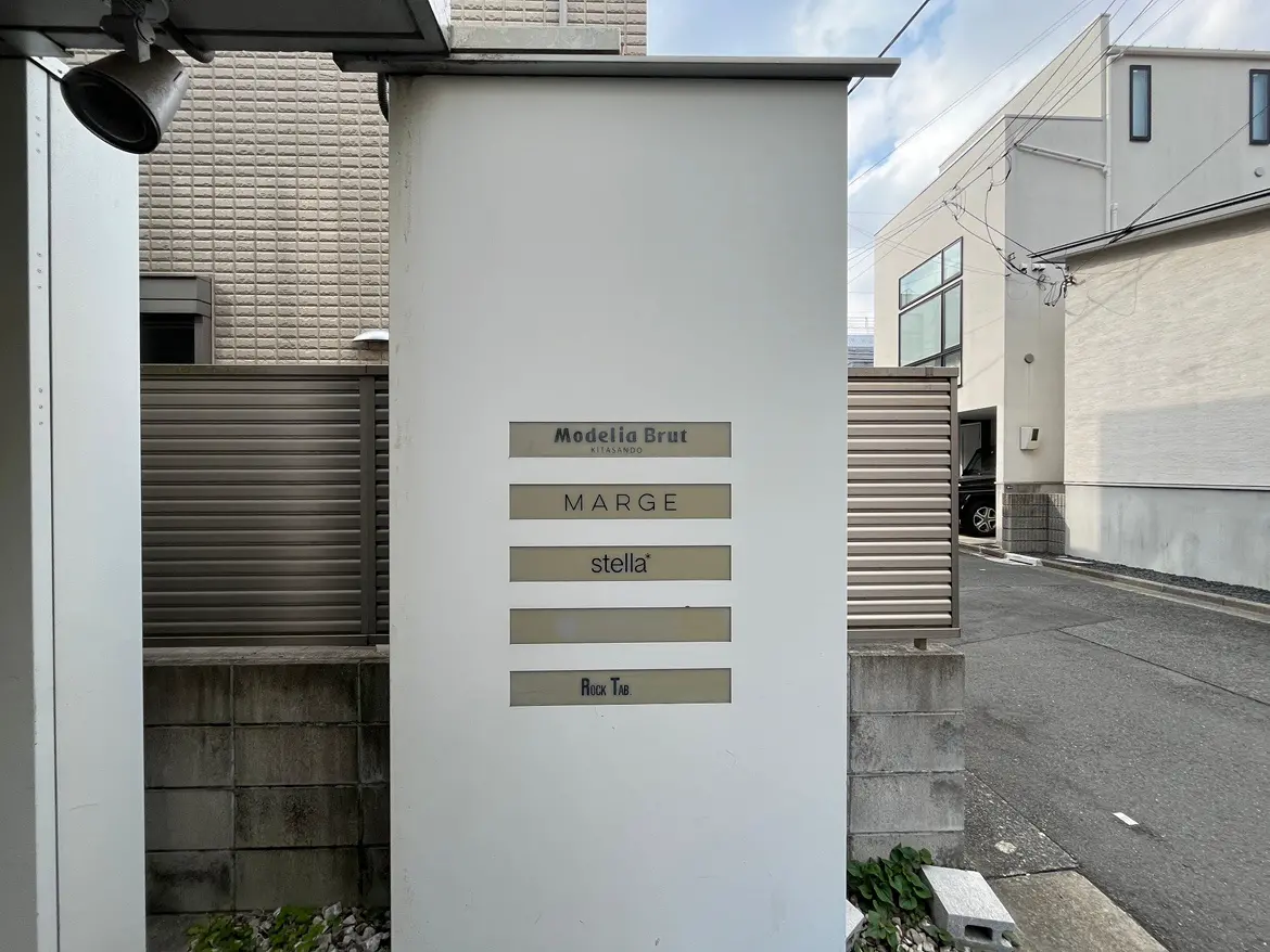 - モダンなデザインの建物の入口看板、店舗名「MARGE」と「stella」などのロゴが表示されている景観。