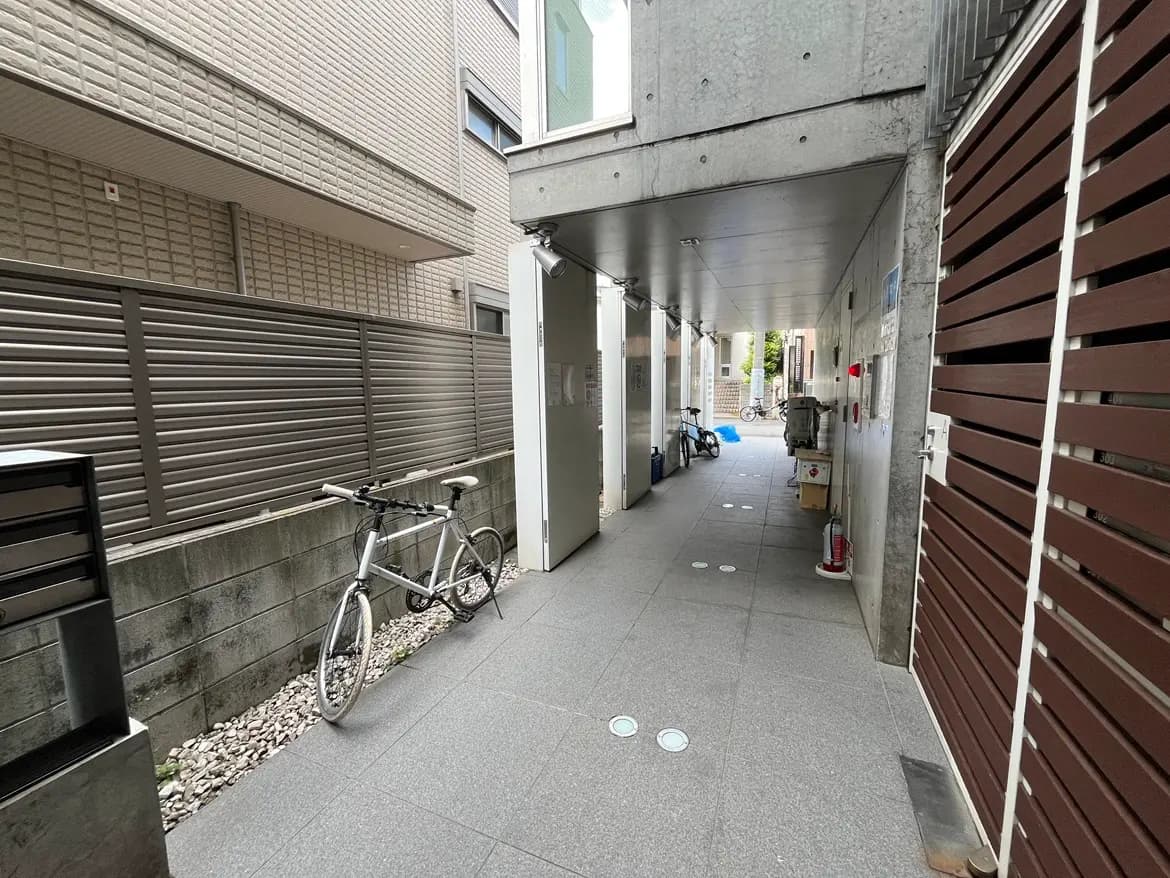 - コンクリート製のアーケード、隣接する建物の壁と郵便受け、白い自転車が置かれた通路の風景