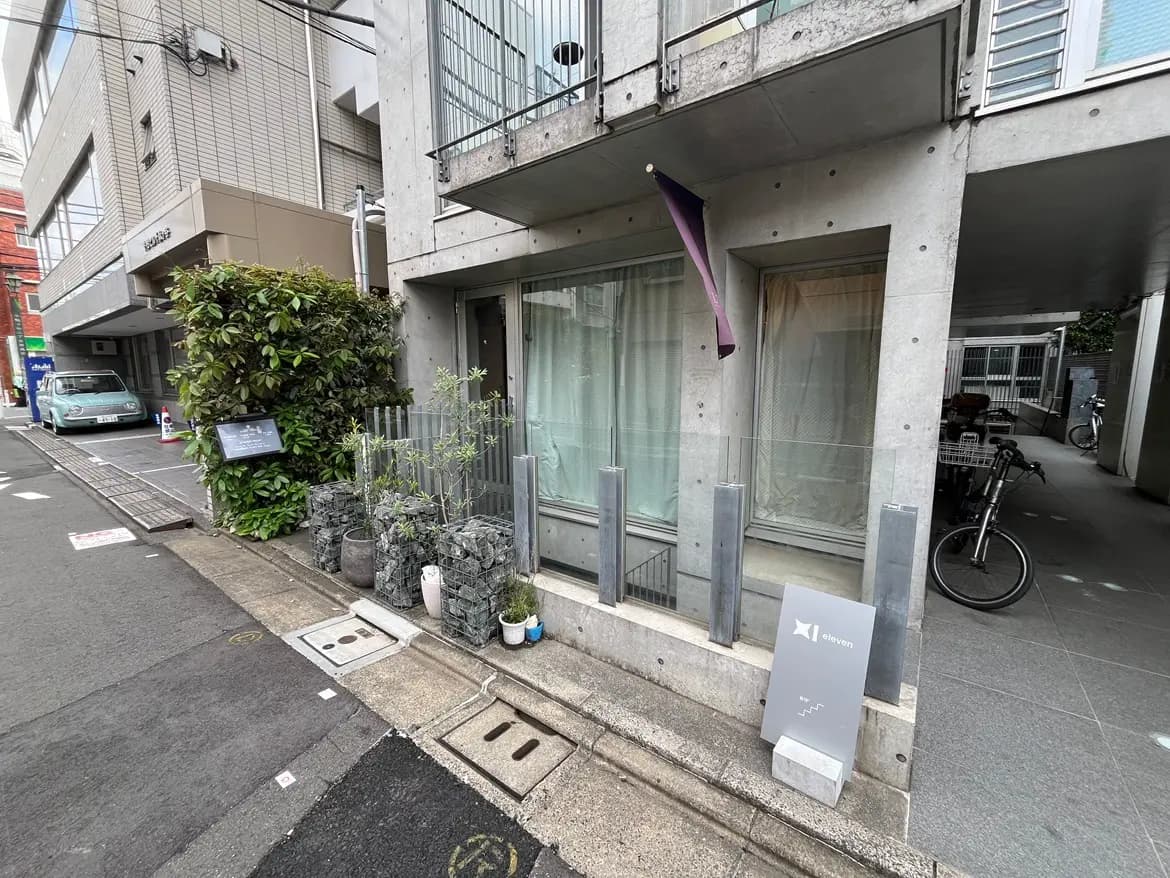 - コンクリート風の現代的な建物の外観、植栽や自転車が置かれたエントランス周辺の様子