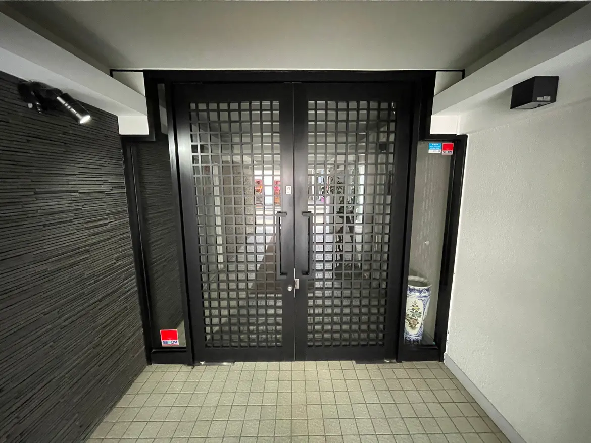 モダンなデザインの建物入り口、黒い格子デザインの扉、照明付きの玄関ホール