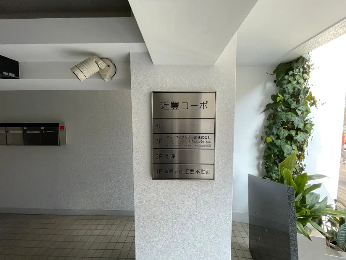 ビルのエントランスに設置された案内板、室内防犯カメラと観葉植物、整理された郵便受け