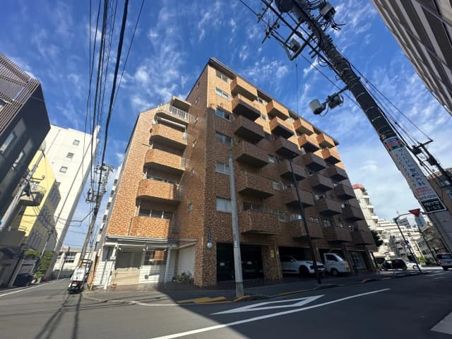 都市の風景、茶色のレンガ調のマンション、晴れた日の青空、街路樹、電信柱と配線