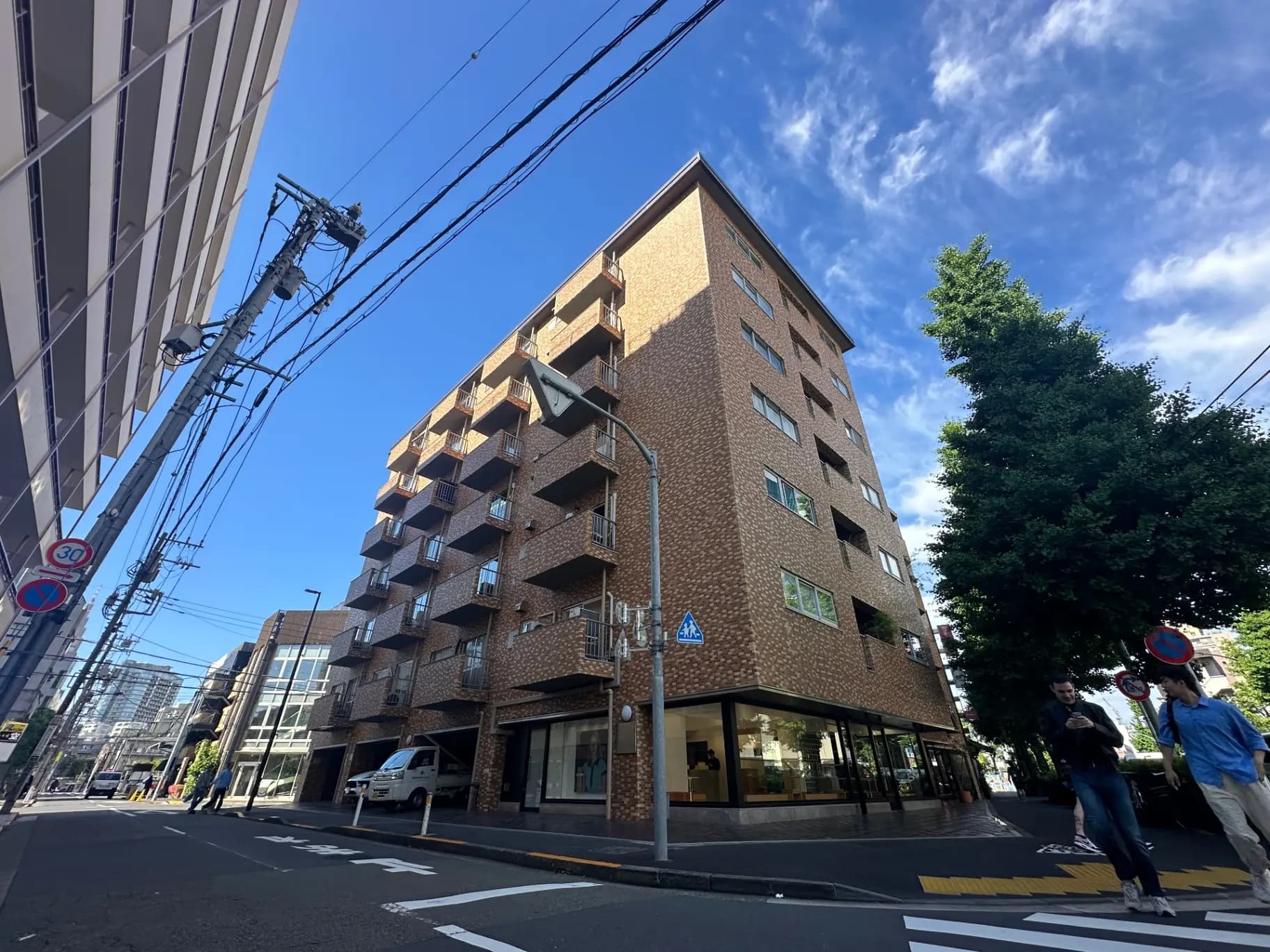日差しが明るい都市の角に位置するモダンな外観のレンガ造りのアパートビル、歩行者と街路樹が見える都会の風景