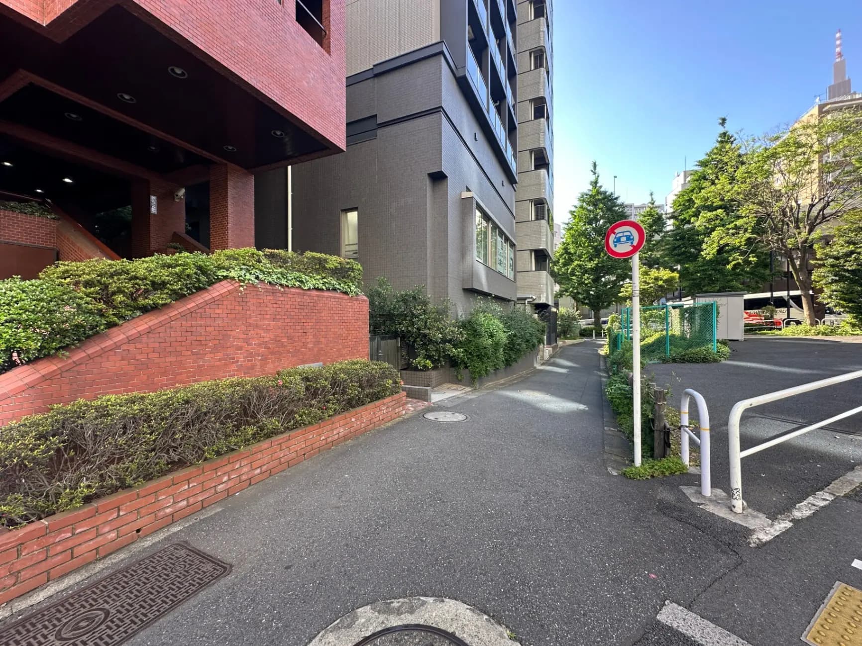 日本の都市部の住宅街、緑豊かな歩道、レンガ造りの壁と建物、晴れた日の街並み