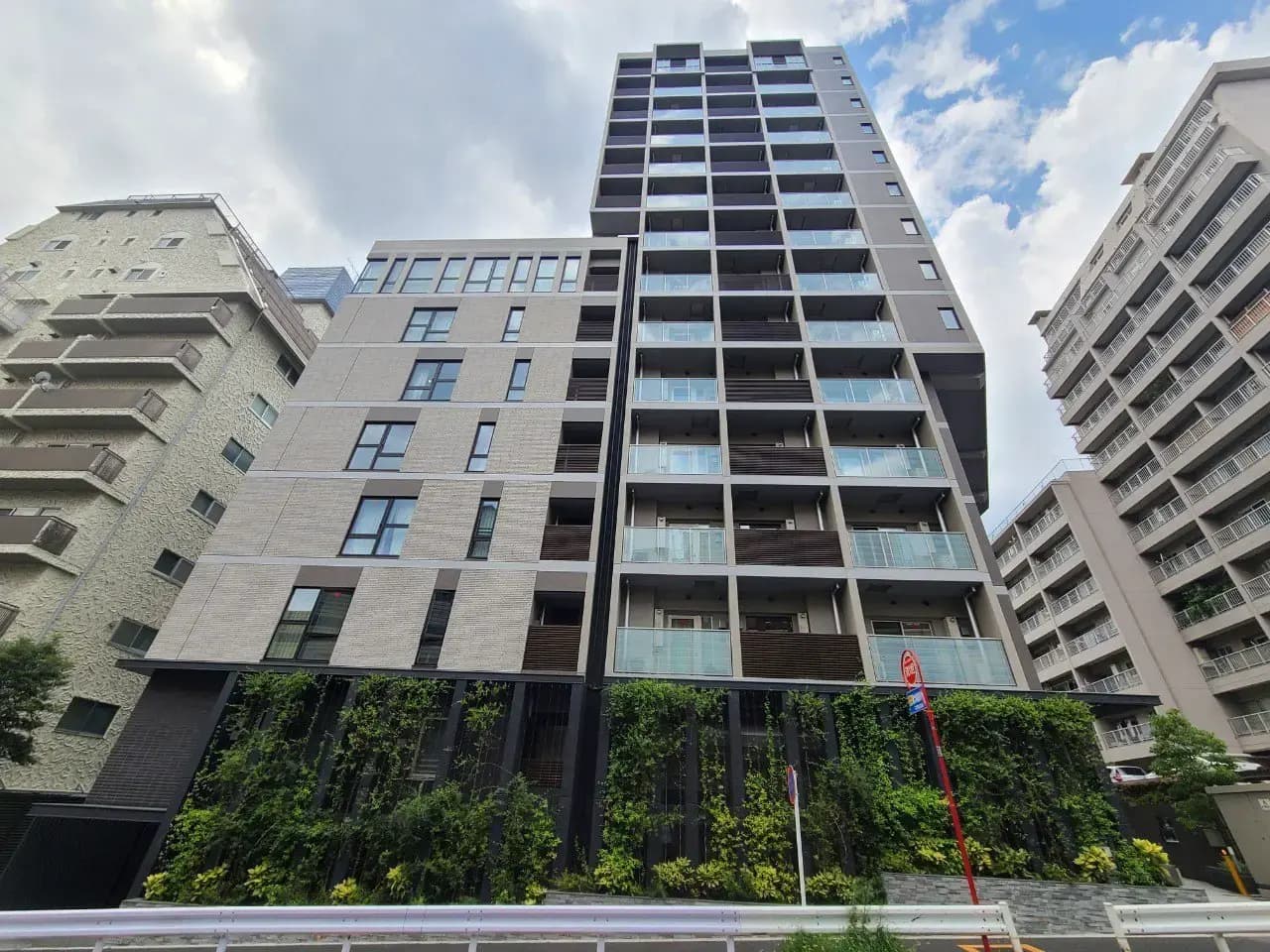 都市のモダンなマンションの外観、緑豊かな壁面、晴れた日の青空と高層建築