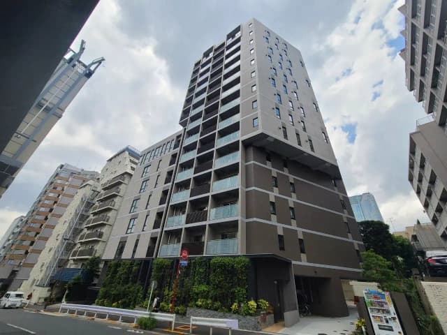 現代的な外観の都市型マンション、くもり空にそびえる高層ビル、緑化された歩道