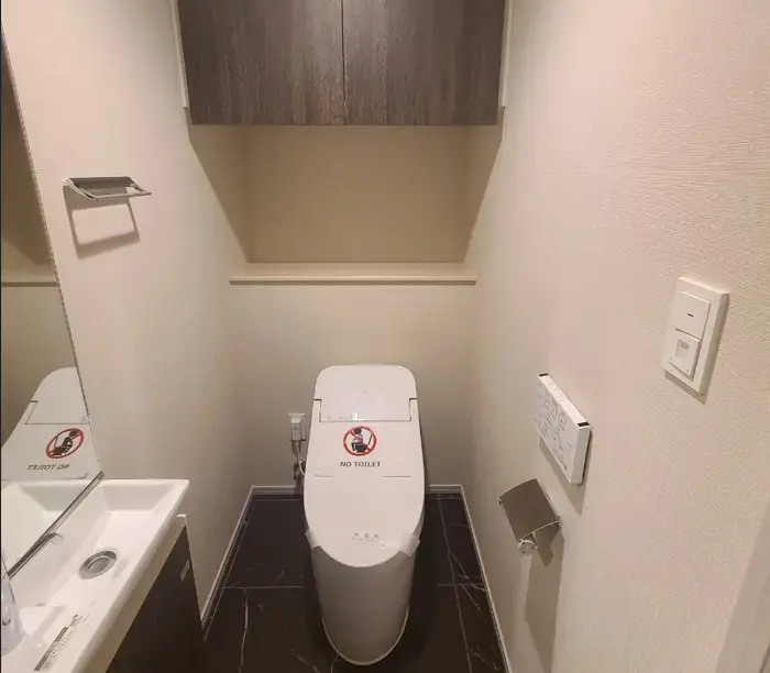 シンプルなデザインのトイレルーム、ウォシュレット付き便座、手洗い器具、暖かい色の壁