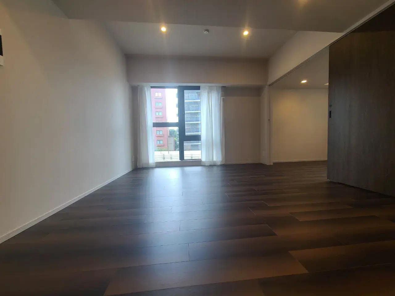 明るい自然光が差し込む広々とした空の部屋、ダークブラウンの木製フローリング、モダンな建築デザイン