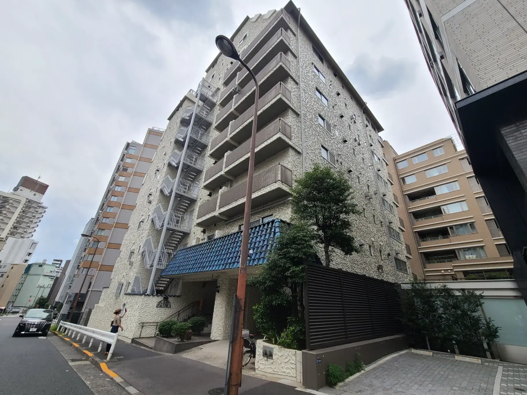 都市のアパート建物と歩行者、筋模様の壁面デザイン、外階段とストリートランプ