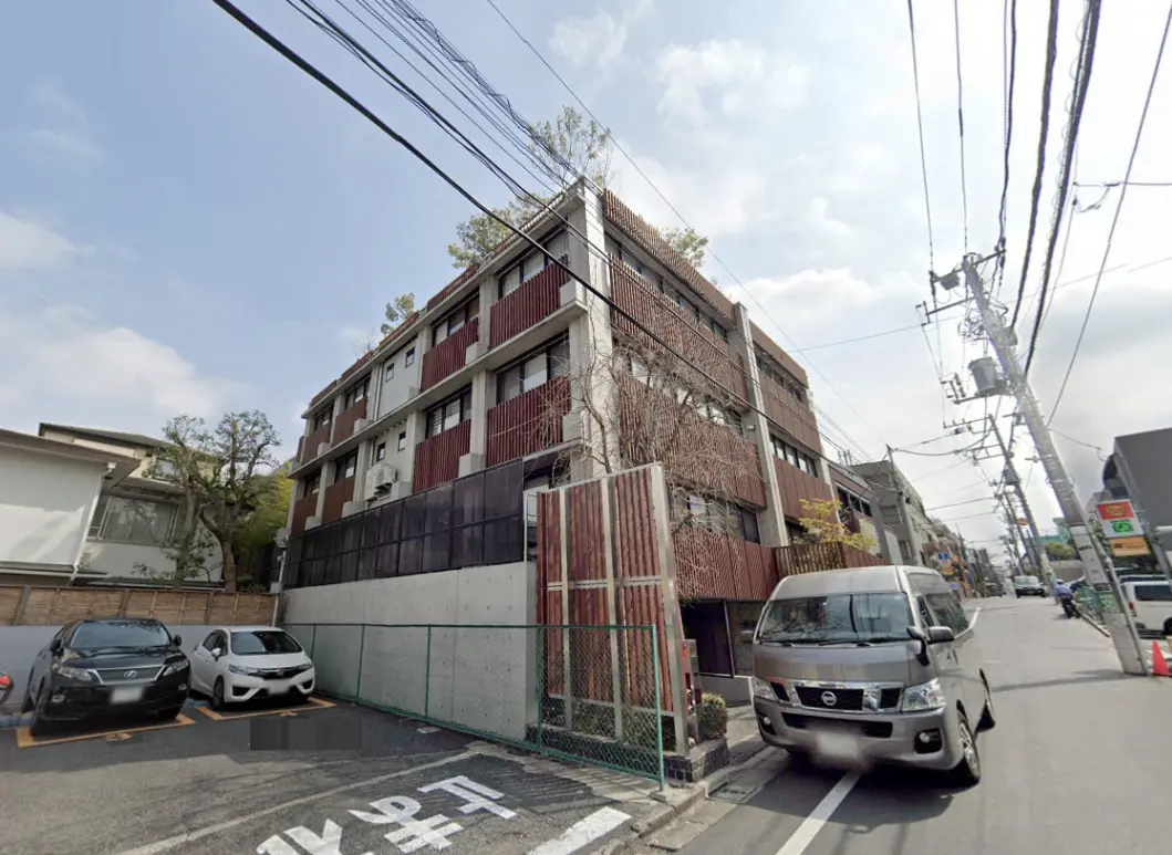 - 都市の住宅街にあるモダンなアパートメントビル、駐車場と周囲の街並みが見える風景