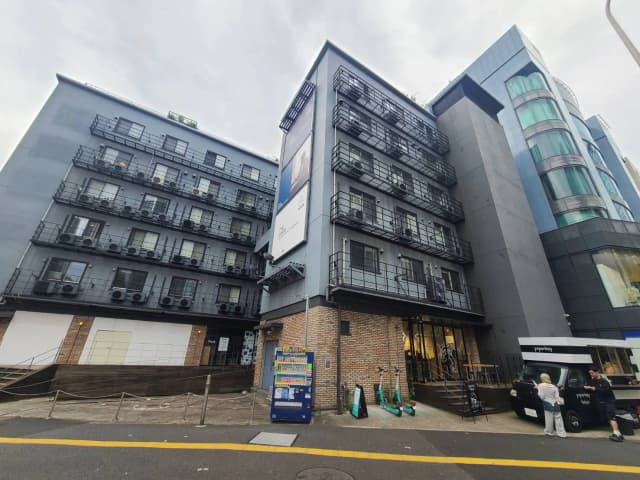 都市の角に建つモダンな建築のアパートメント、エントランスと多数のエアコン外部ユニットが見える外観