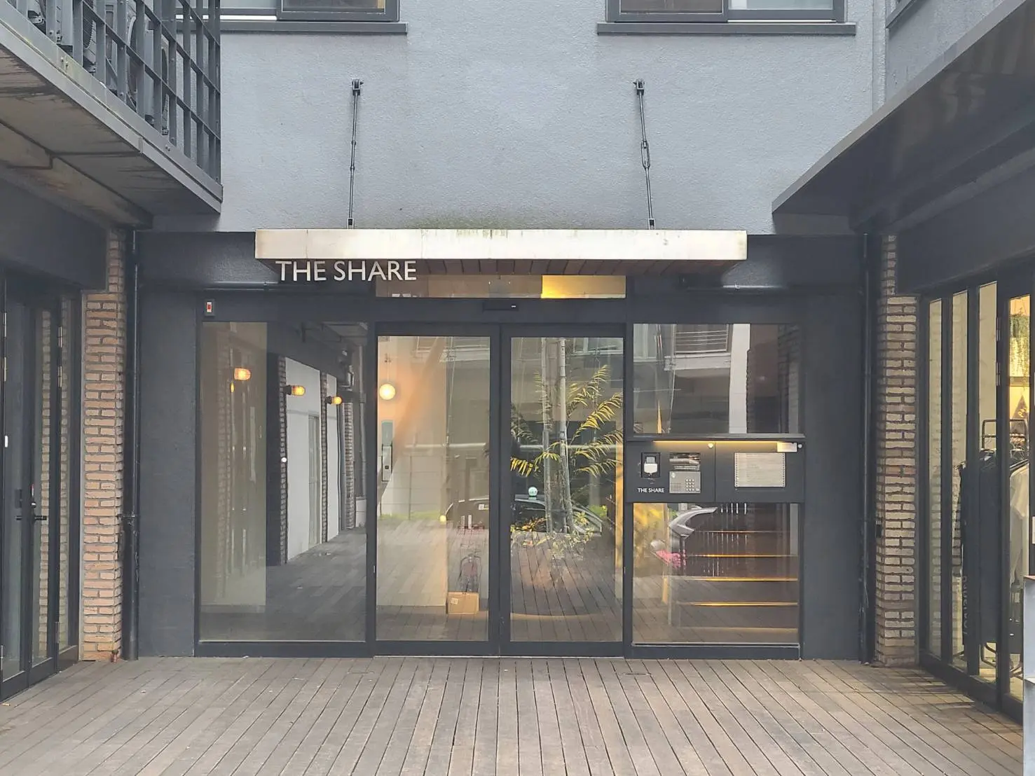 モダンな外観のオフィスビル入口、ブラックとブリックの装飾、ガラスドアに「THE SHARE」と記された看板
