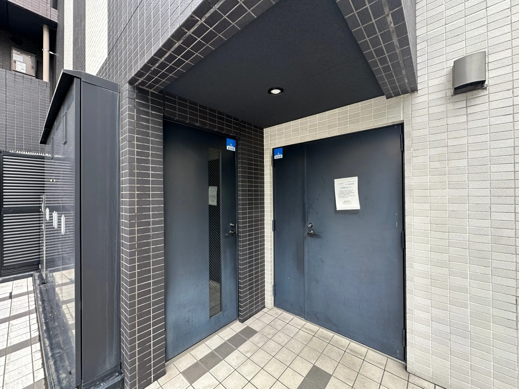 ダークトーンのタイル張りの建物入口と青いドア、バリアフリー対応のトイレ案内看板が見える外観