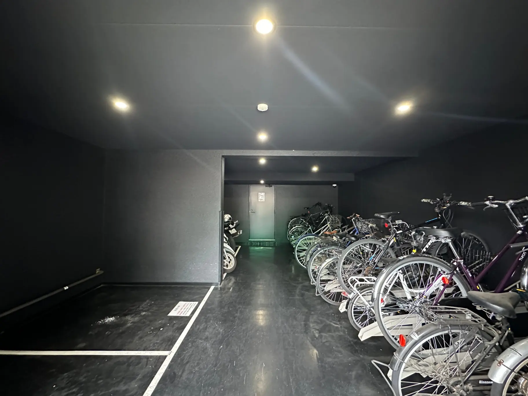 照明が明るく綺麗に整列された自転車駐輪スペース、奥にモーターバイク、清潔感のある都市型駐輪場内部
