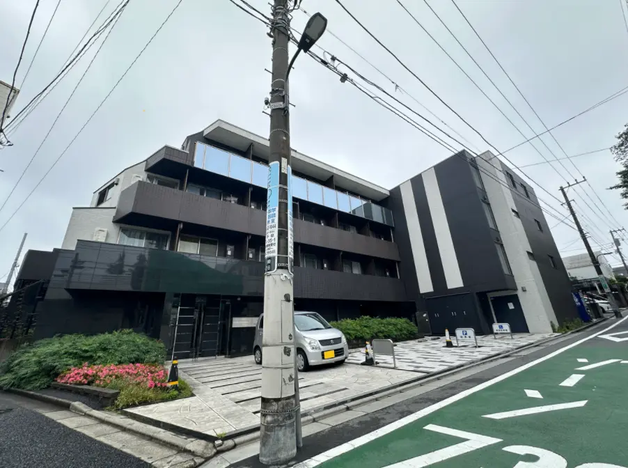 現代的なデザインの黒とグレーの外装を持つ都市型オフィスビル、前面に駐車スペースと歩道、街路樹と電信柱が見える外観