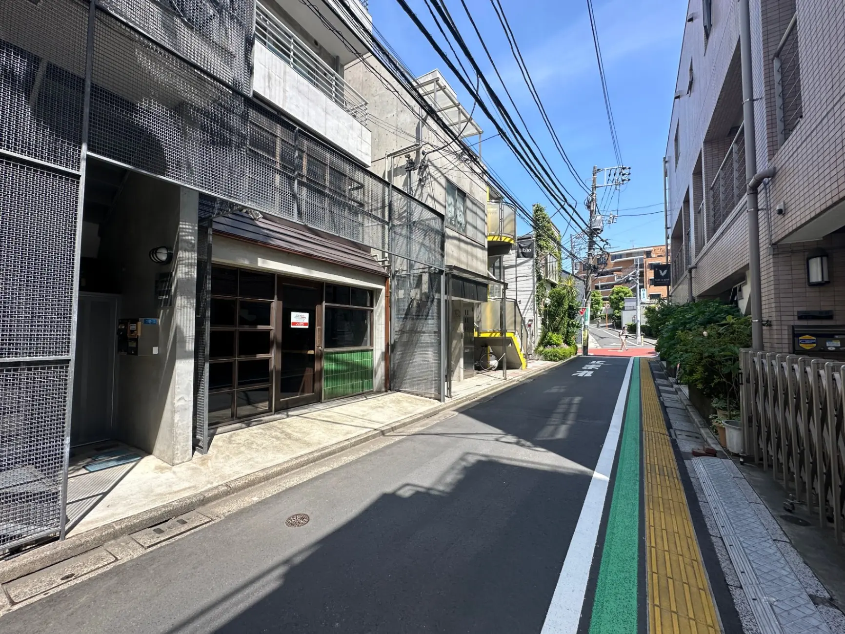 都会の小道と商店、晴れた日の青空、歩行者のための黄緑色のラインが引かれたアスファルト
