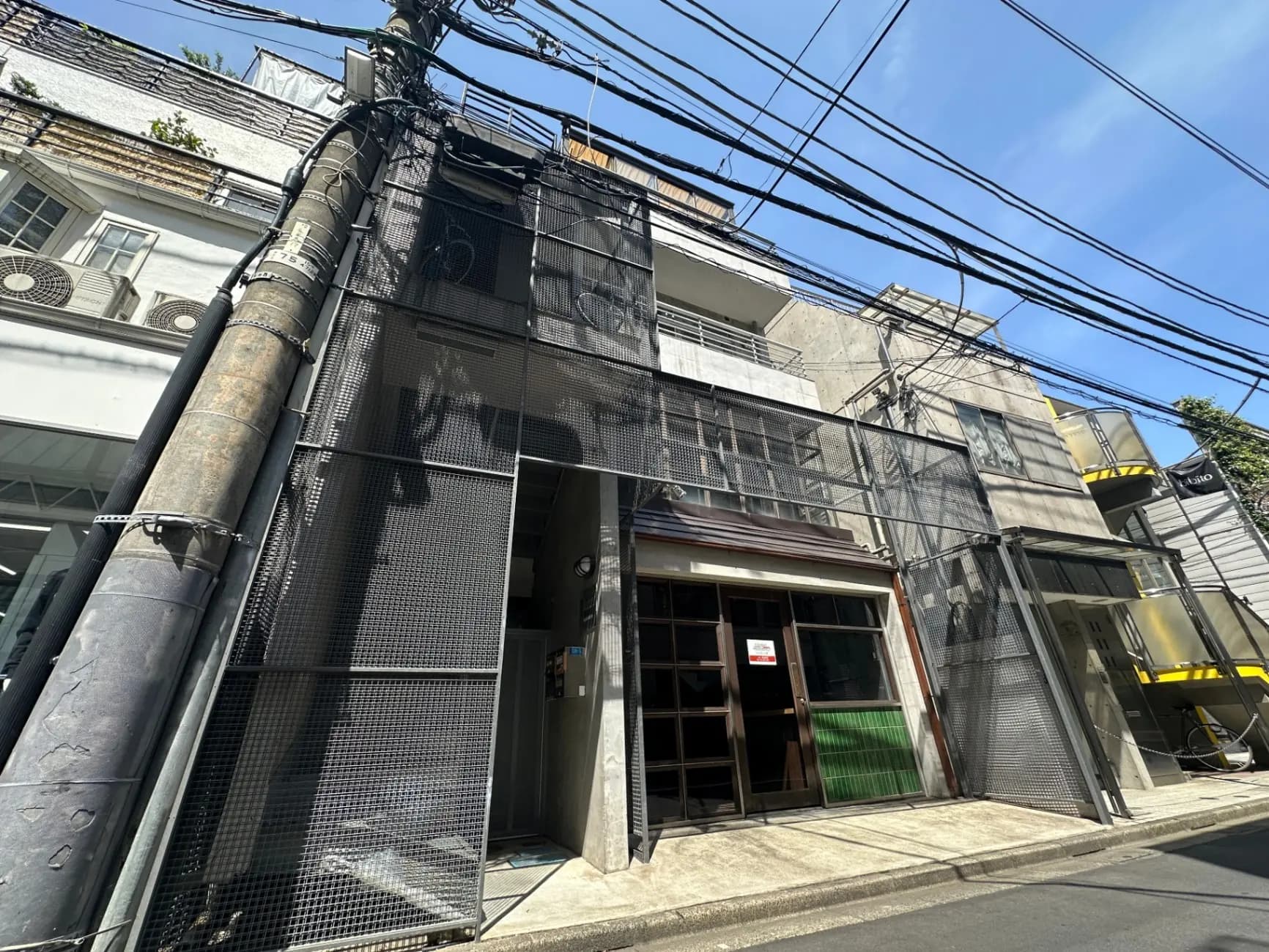 日差しが降り注ぐ都市の通りにあるモダンな金網のファサードを持つ建物、電柱と多くの電線が見える景観