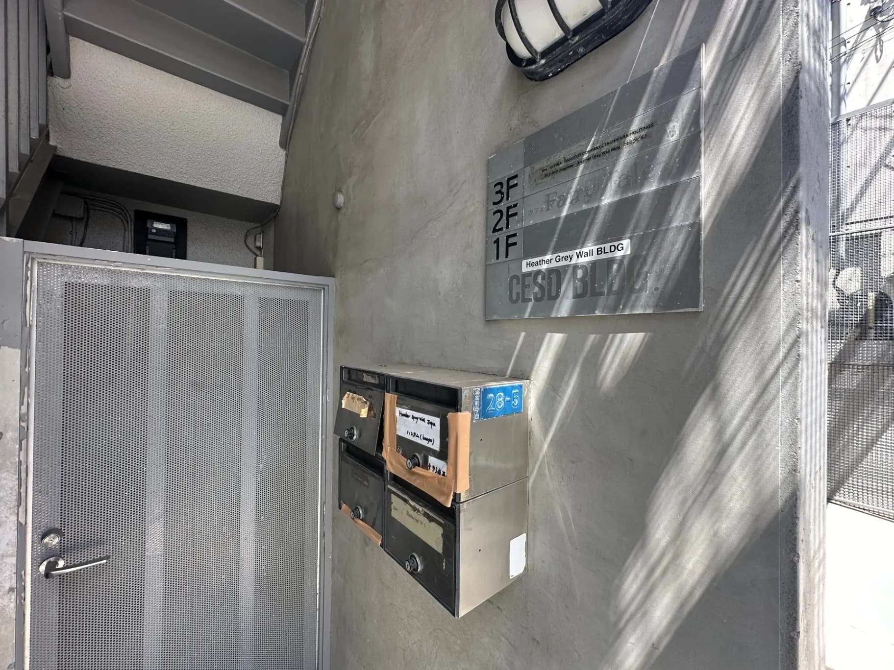 都会の建物入口、コンクリート壁に固定された郵便受けと階層表示、日光が映る外観