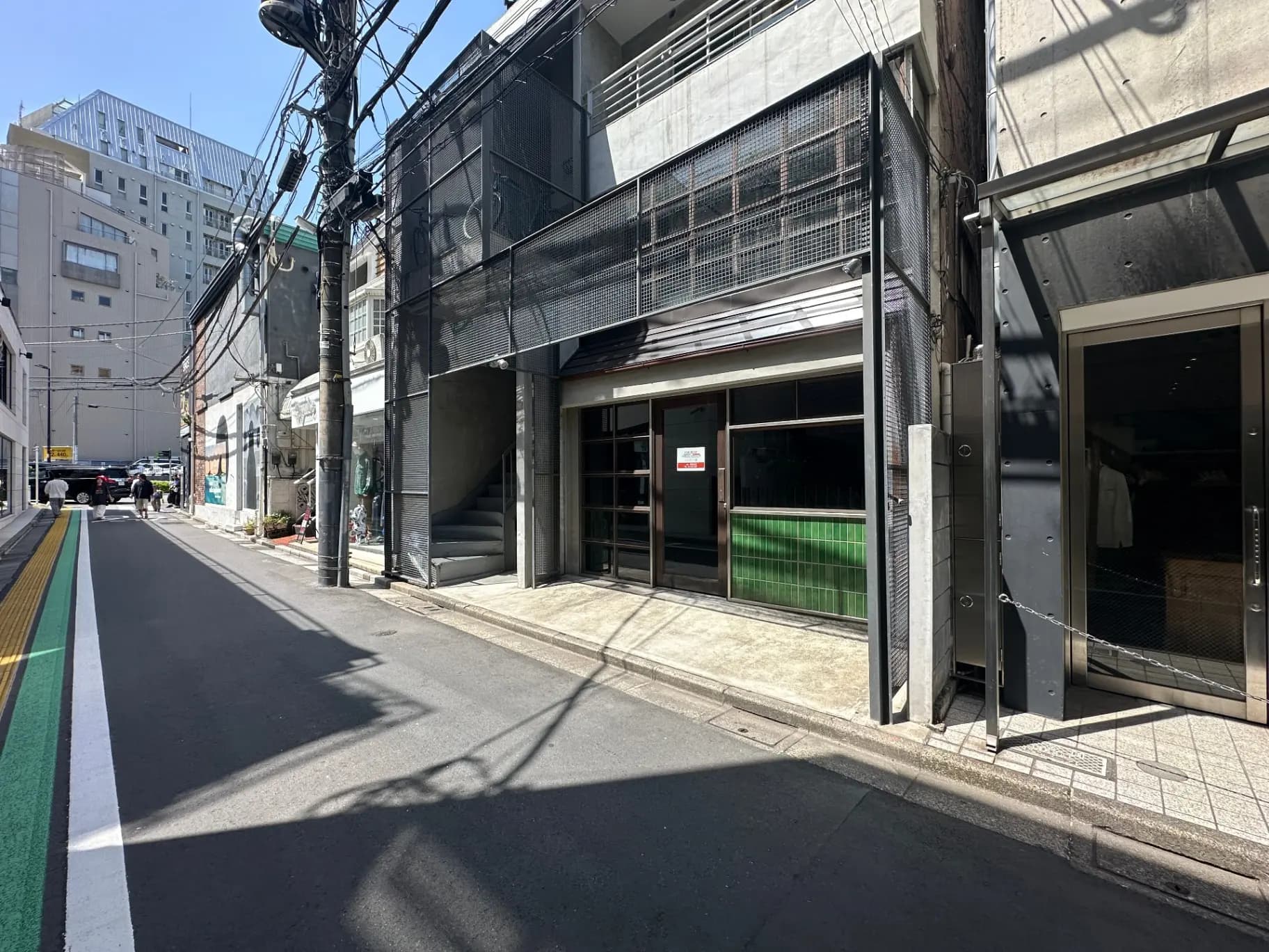 日本の都市部の通り、晴れた日の光が反射するビルと道路、電線が交差する空の風景