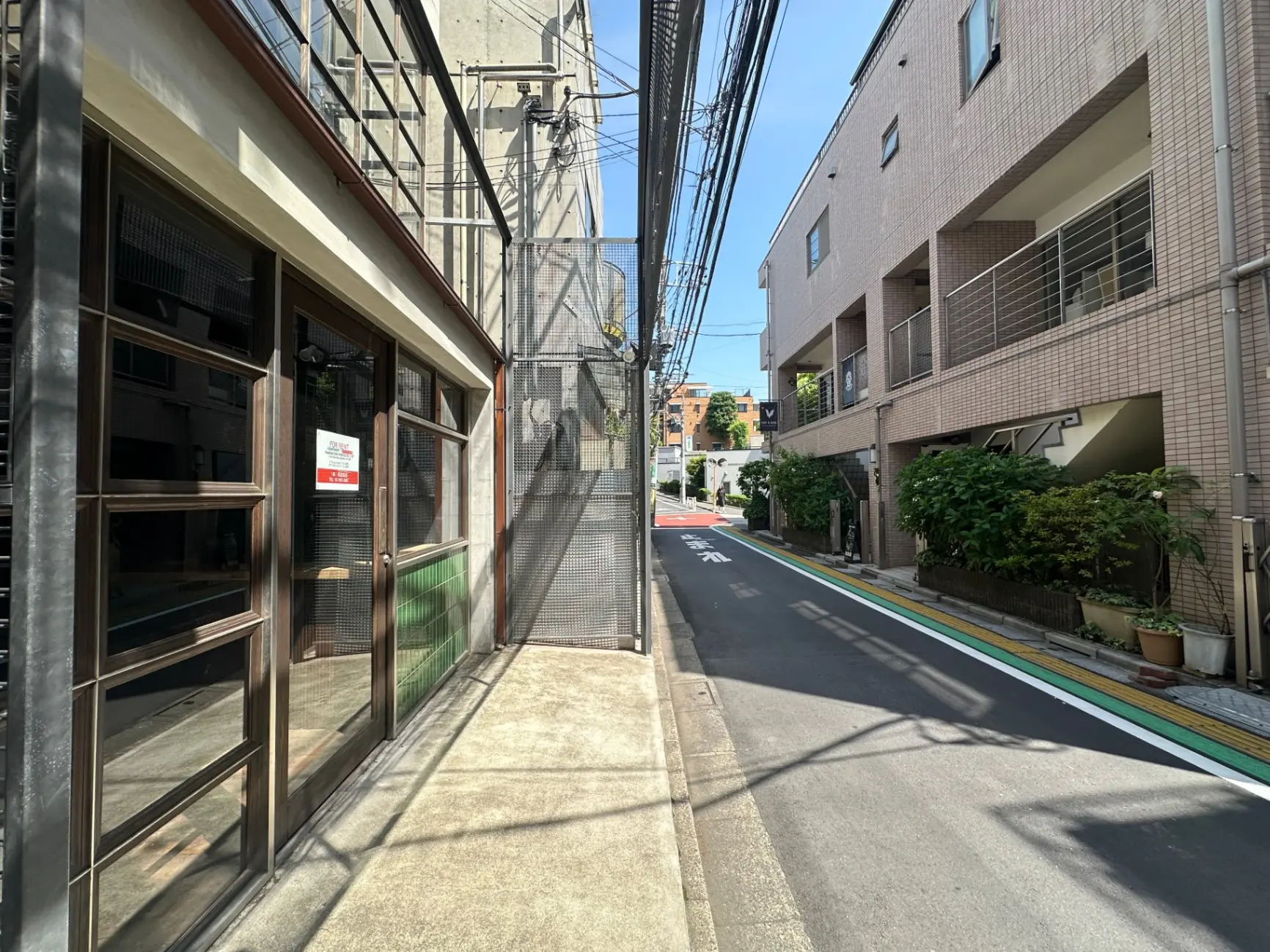 晴れた日の日本の住宅街の風景、左側にはガラス窓のあるビルの入口、右側にはアパートと植物
