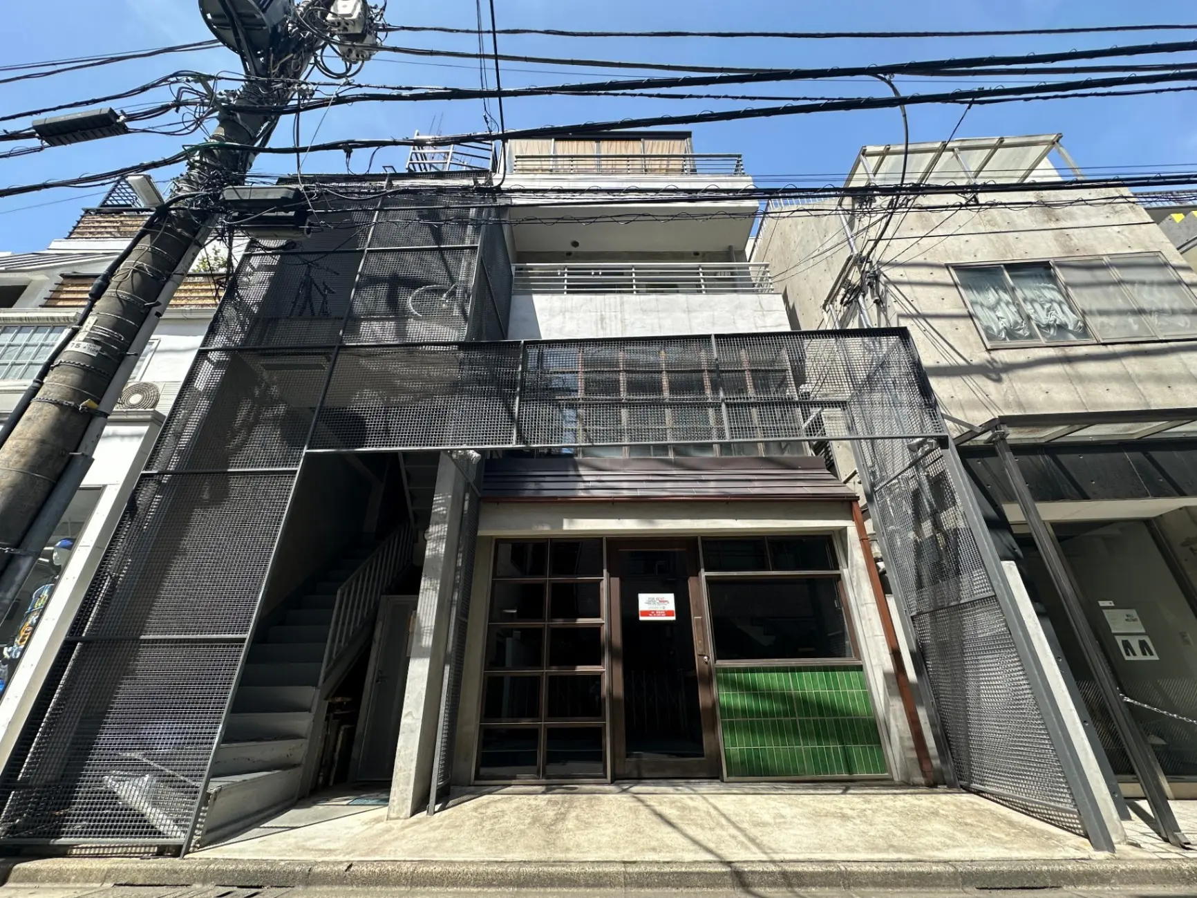 都市の風景、日本の都市部にある現代的な建築スタイルのビルの外観、金属製のメッシュが印象的な階段とエントリーウェイ