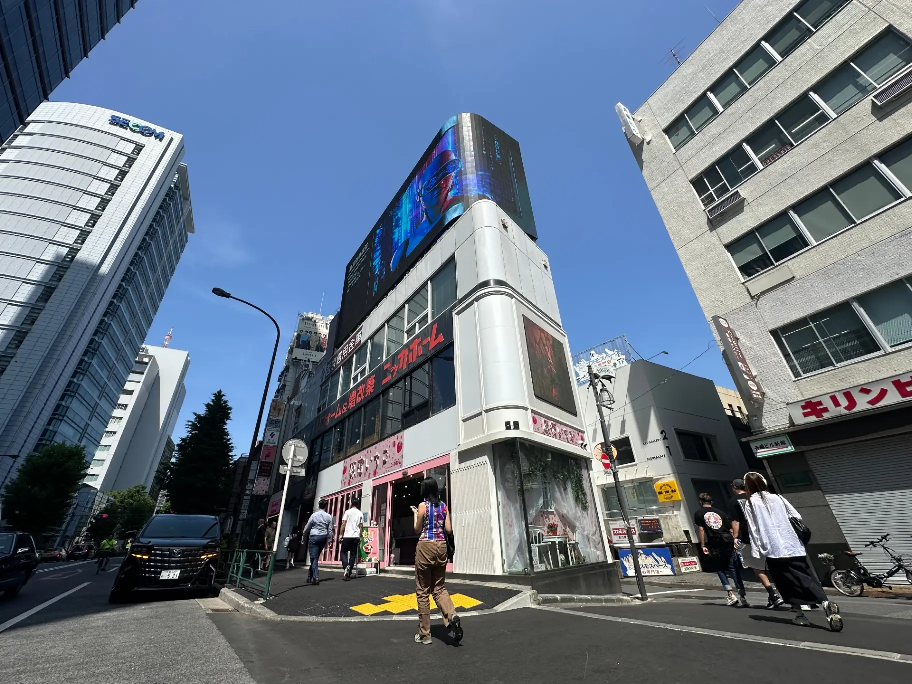 日差しが明るい都市の交差点、歩行者が歩く歩道、ビルにデジタルサイネージ広告が映える風景