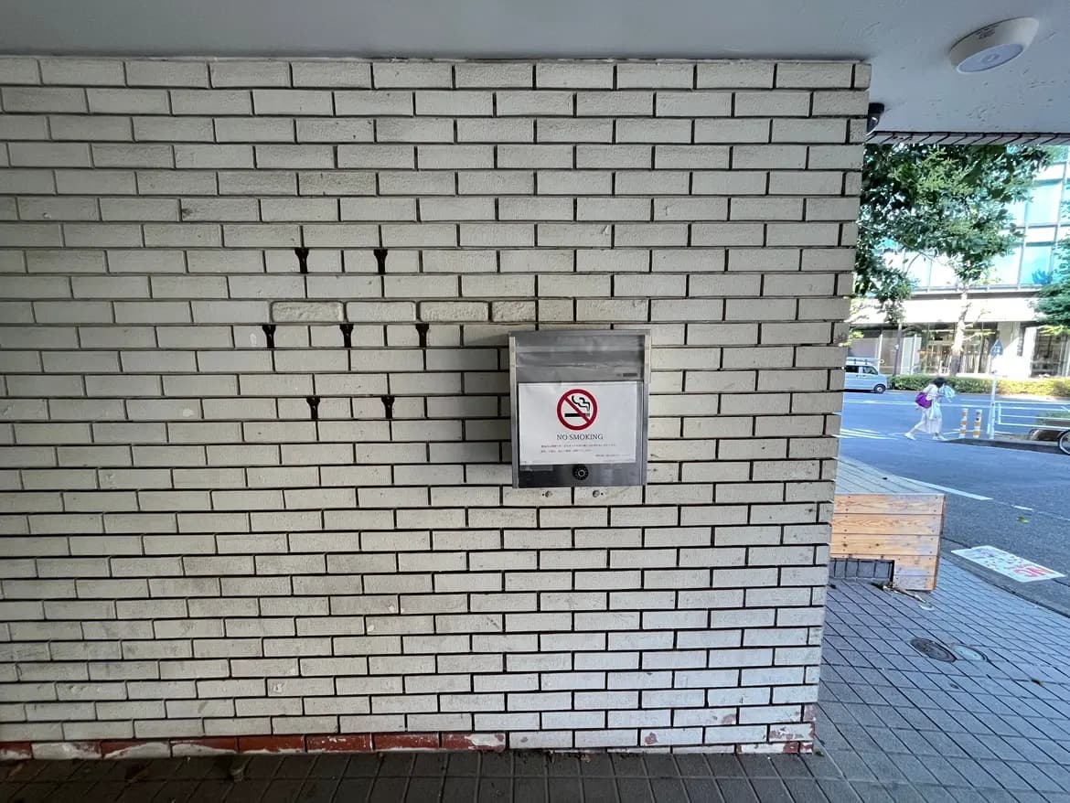 - 白いレンガの壁に設置された禁煙の表示がある灰皿、周囲には街の景色が広がる商業エリア