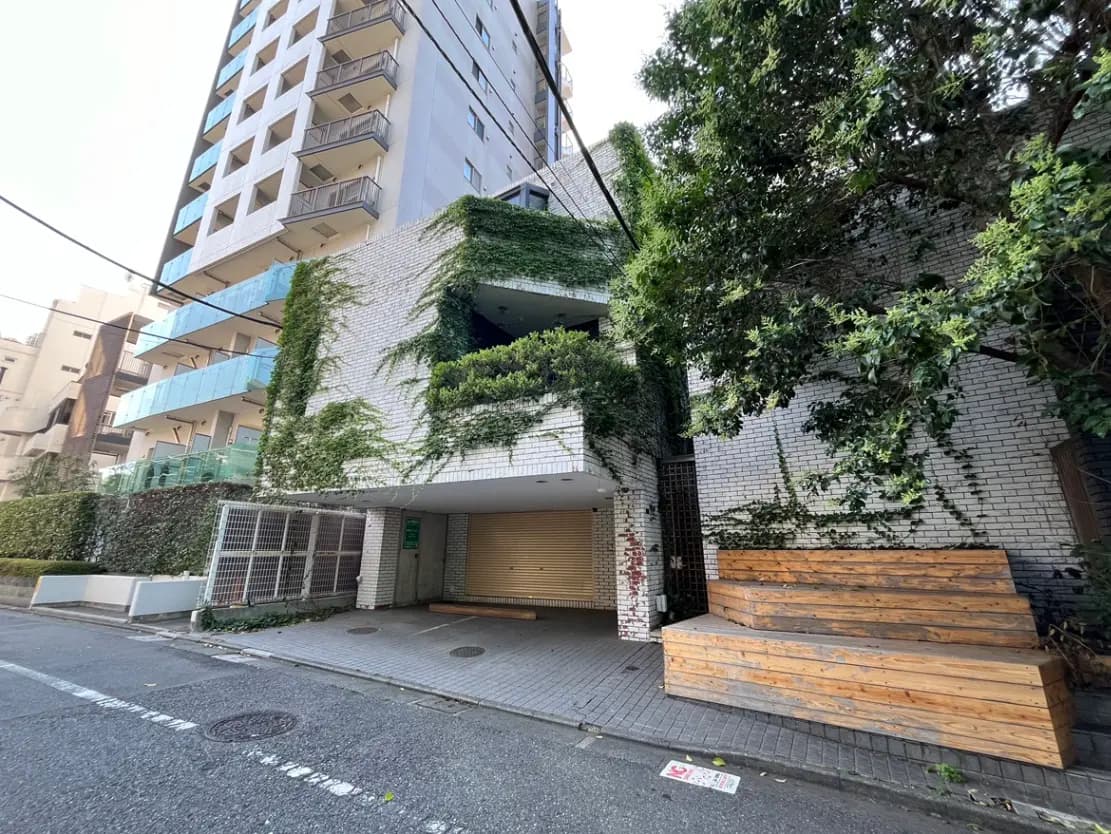 - 緑に覆われたオシャレなマンションの外観、自然素材のベンチが設置されたエントランス周りの風景