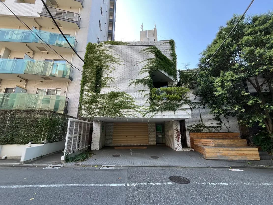 - 緑に覆われたモダンな外観の建物、広いエントランスと木製デッキがある街並みの風景