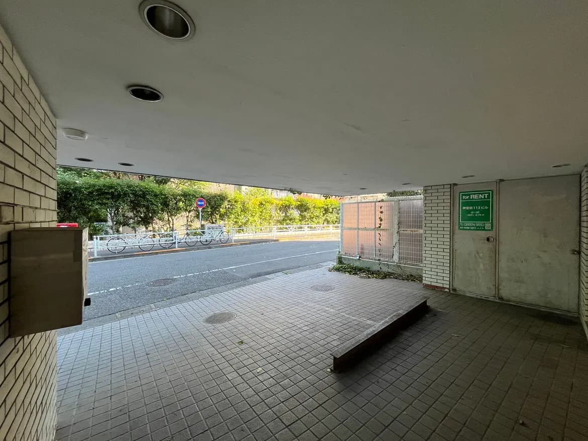 - 開放的なビルのエントランス、明るいタイルの床、外には自転車が停まっている静かな通りの風景