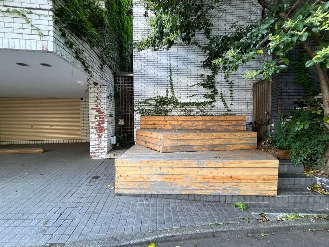 - 緑に囲まれた木製の階段とレンガの壁、メンテナンスが施された屋外のエントランススペース