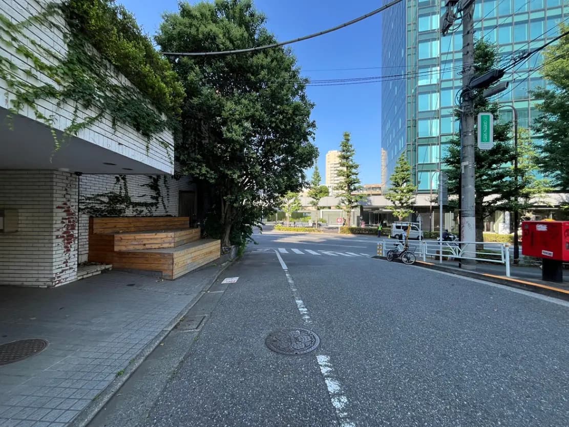 - 緑があふれる街角の風景、木製のベンチとタイル張りの歩道、青空を背景にした現代的なビル群