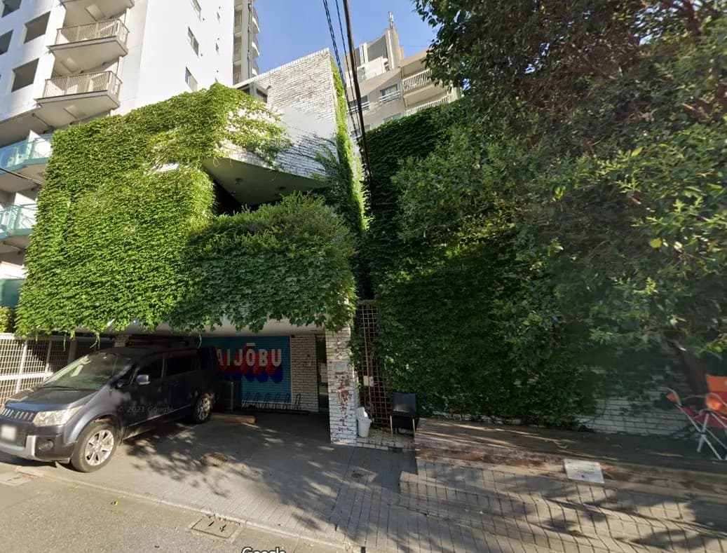 緑の植物で覆われたビルの外観、街角の駐車中の車、入り口にカラフルなロゴのある商業施設