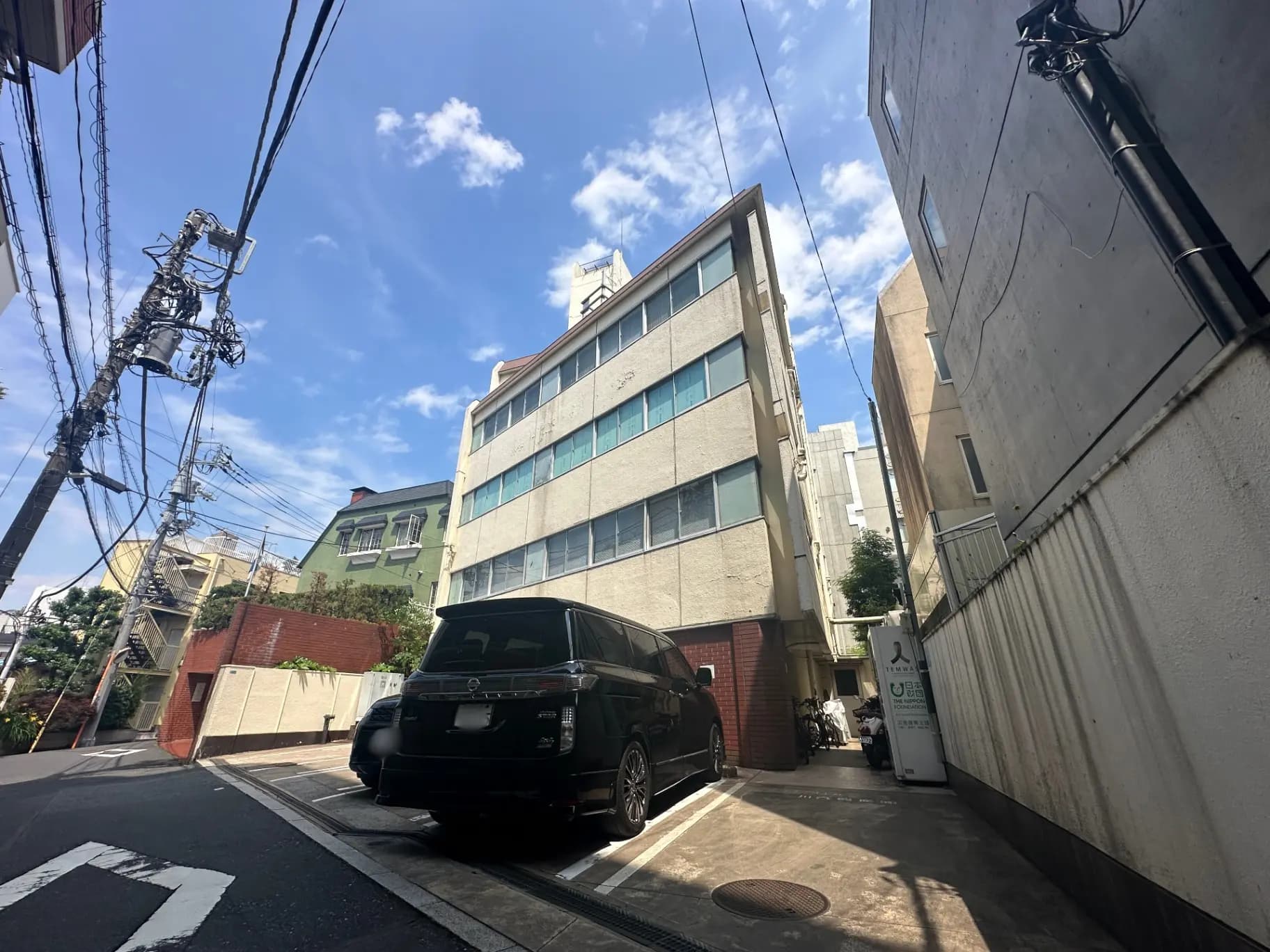 晴れた日の市街地の狭い道、ビルと電柱、停車中の黒い車