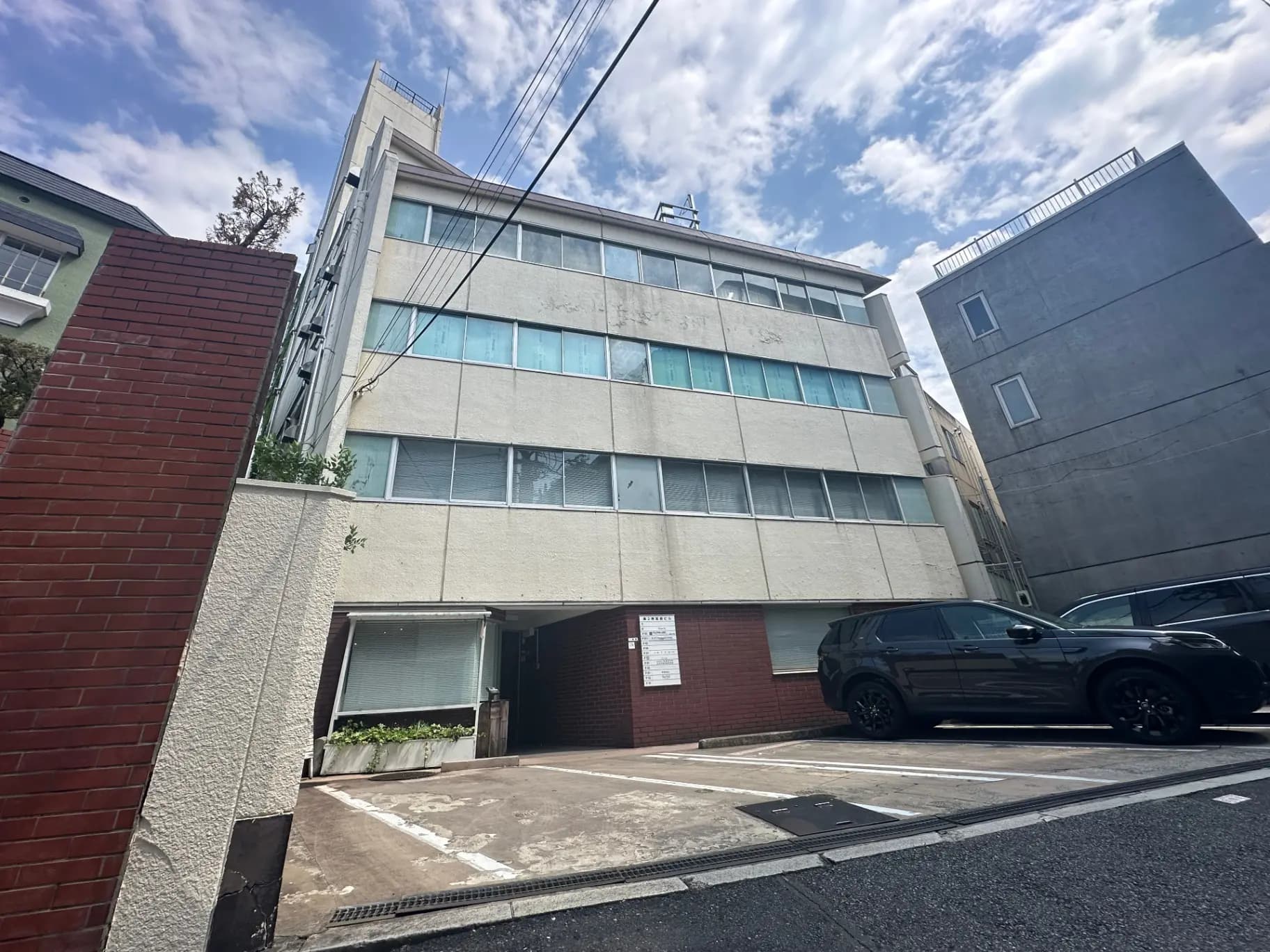 日中の都市風景、モダンな外観のオフィスビルまたはアパート、駐車場にSUV車、晴れた空