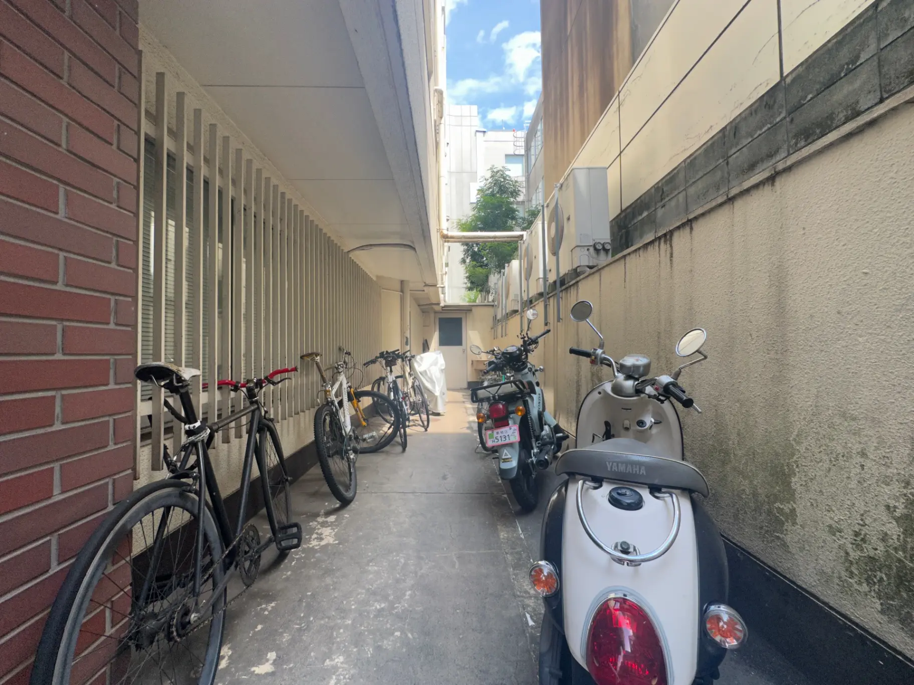 都市のアパートの駐輪所、自転車とスクーターが並ぶ狭い通路