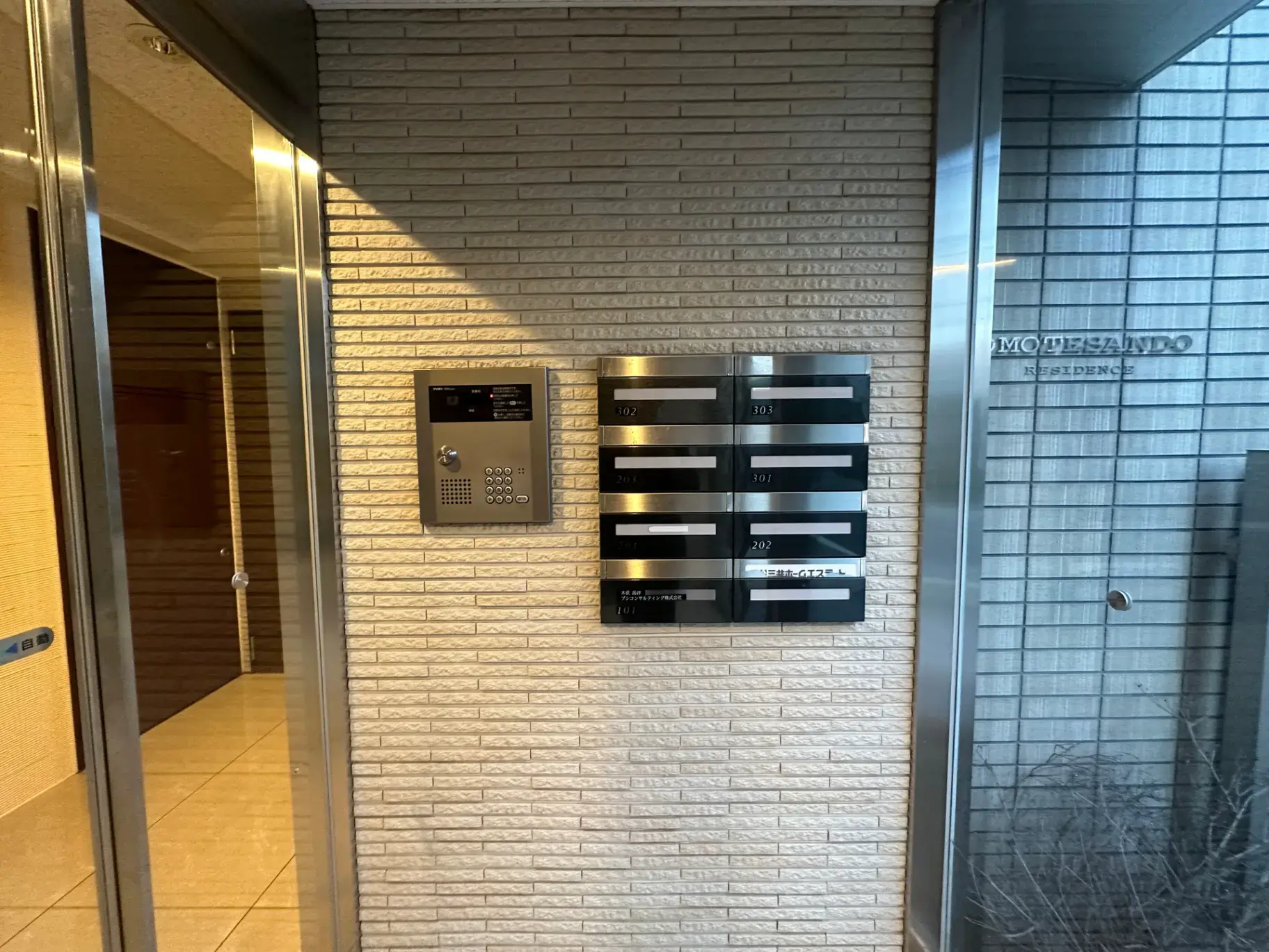 モダンなマンションの入り口、インターホンとポスト、照明とタイルの壁デザイン