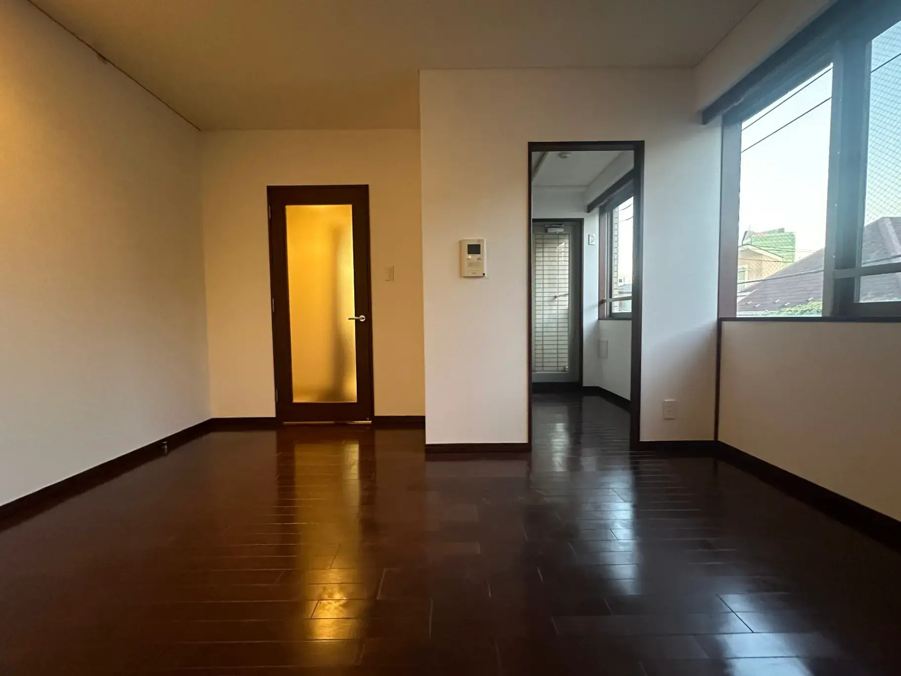 空の部屋と廊下、茶色のフローリング、白い壁、自然光が差し込む窓