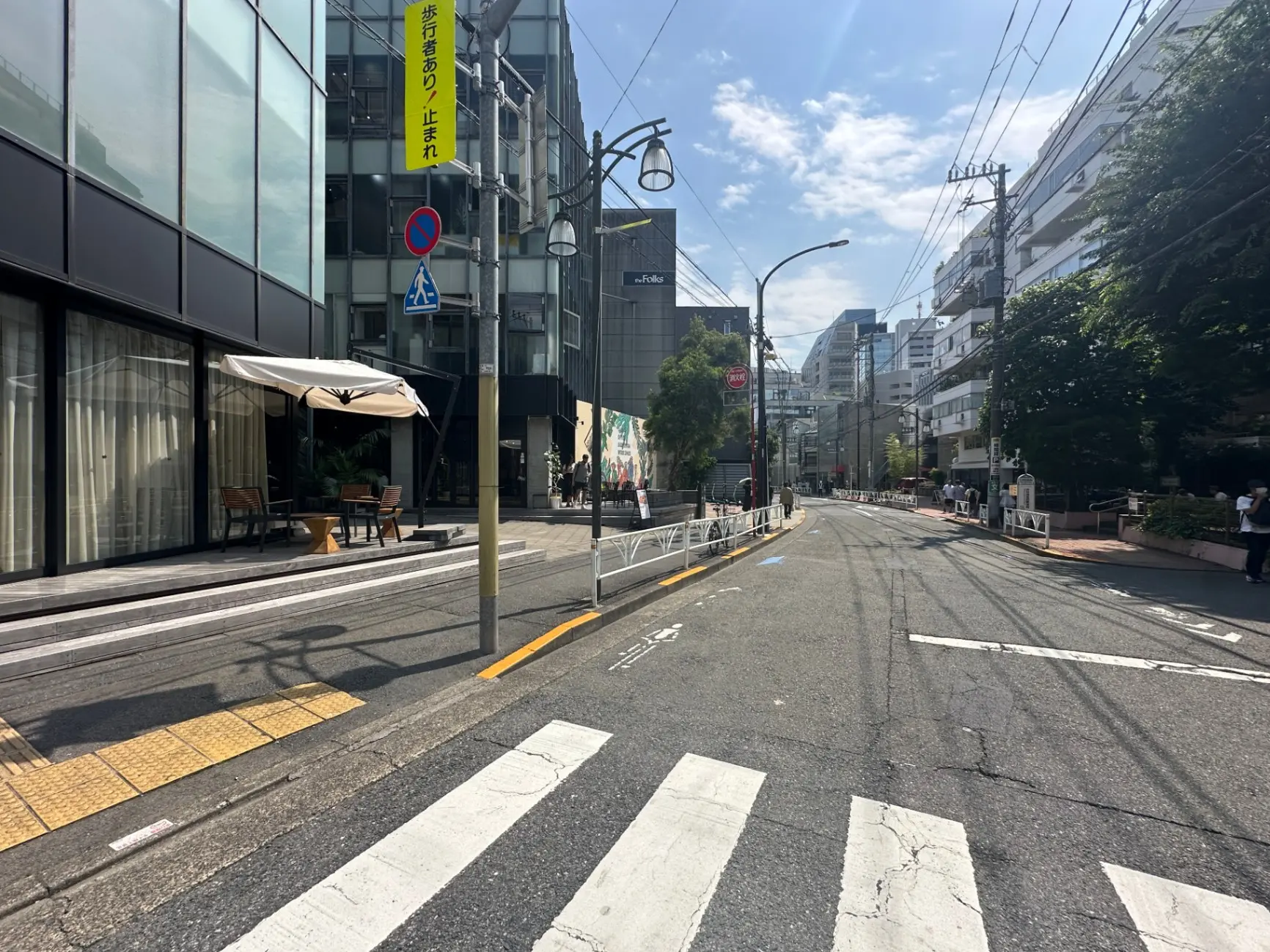 晴れた日の日本の街角、ガラス張りの建物と屋外のカフェ、横断歩道、歩行者と車の通行制限