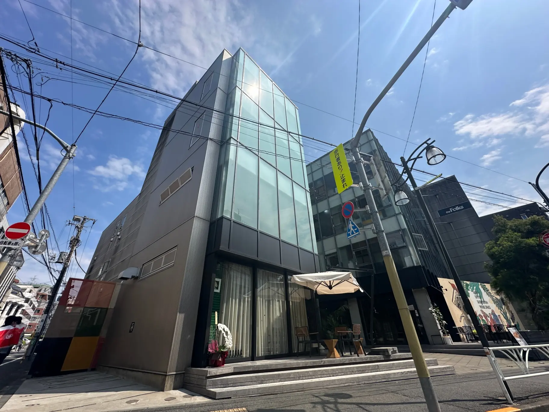 現代的な外観の都市型オフィスビル、ガラスと金属素材を使用したファサード、青空と電線が映るクリアな日中のシーン