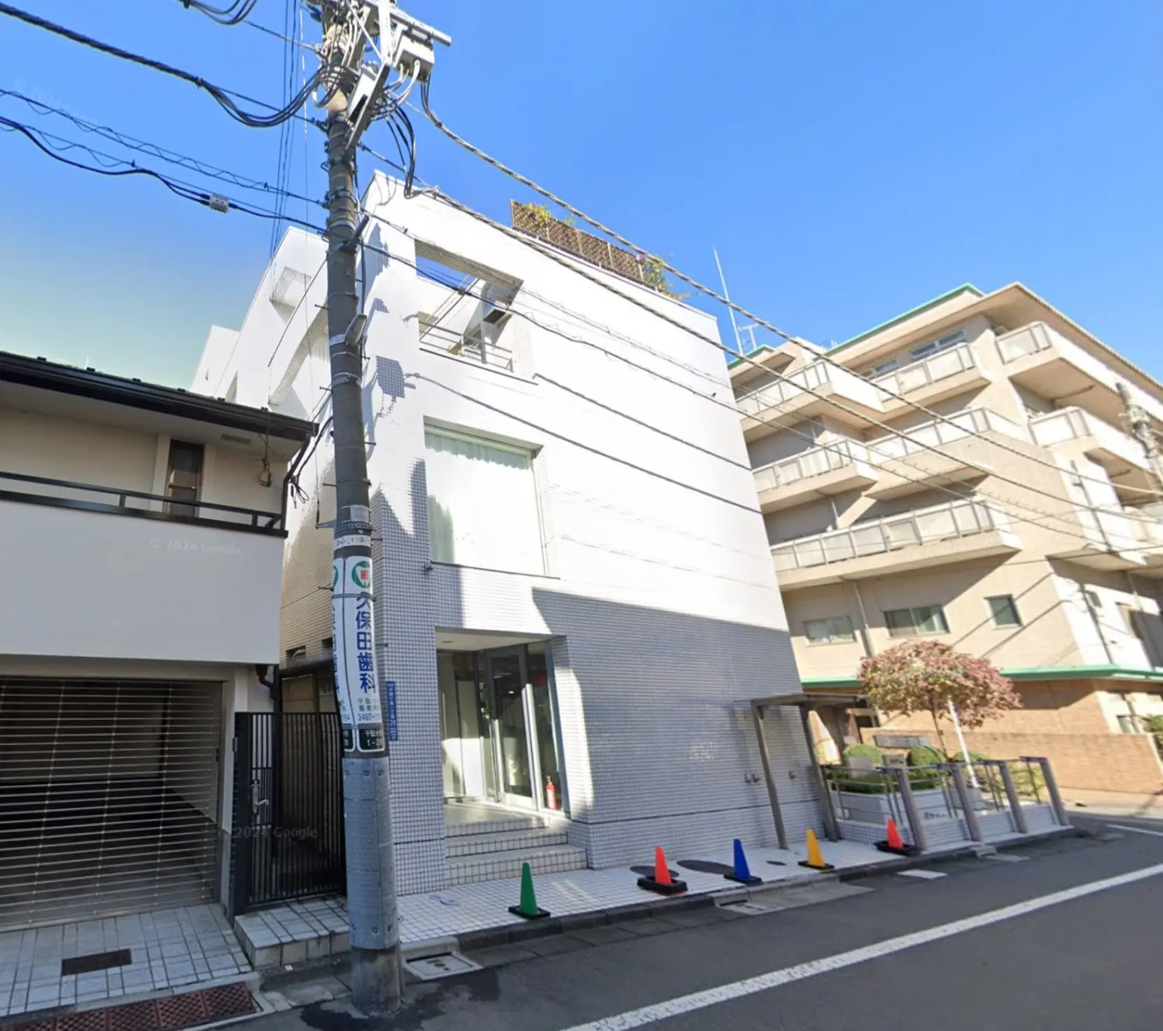 都市の日常風景、白い壁の建物、歩道、道路沿いの樹木と電柱