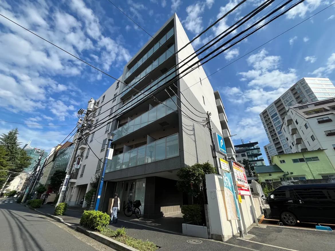 - 高層マンションの外観、晴れた空とワイヤーが交差する様子、周囲に緑と街並みが広がるシーン