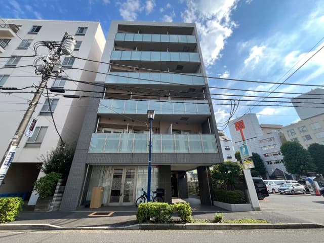 - モダンなデザインの5階建てマンション、バルコニーやガラスの手すりが特徴、青空を背景にした外観の街並み