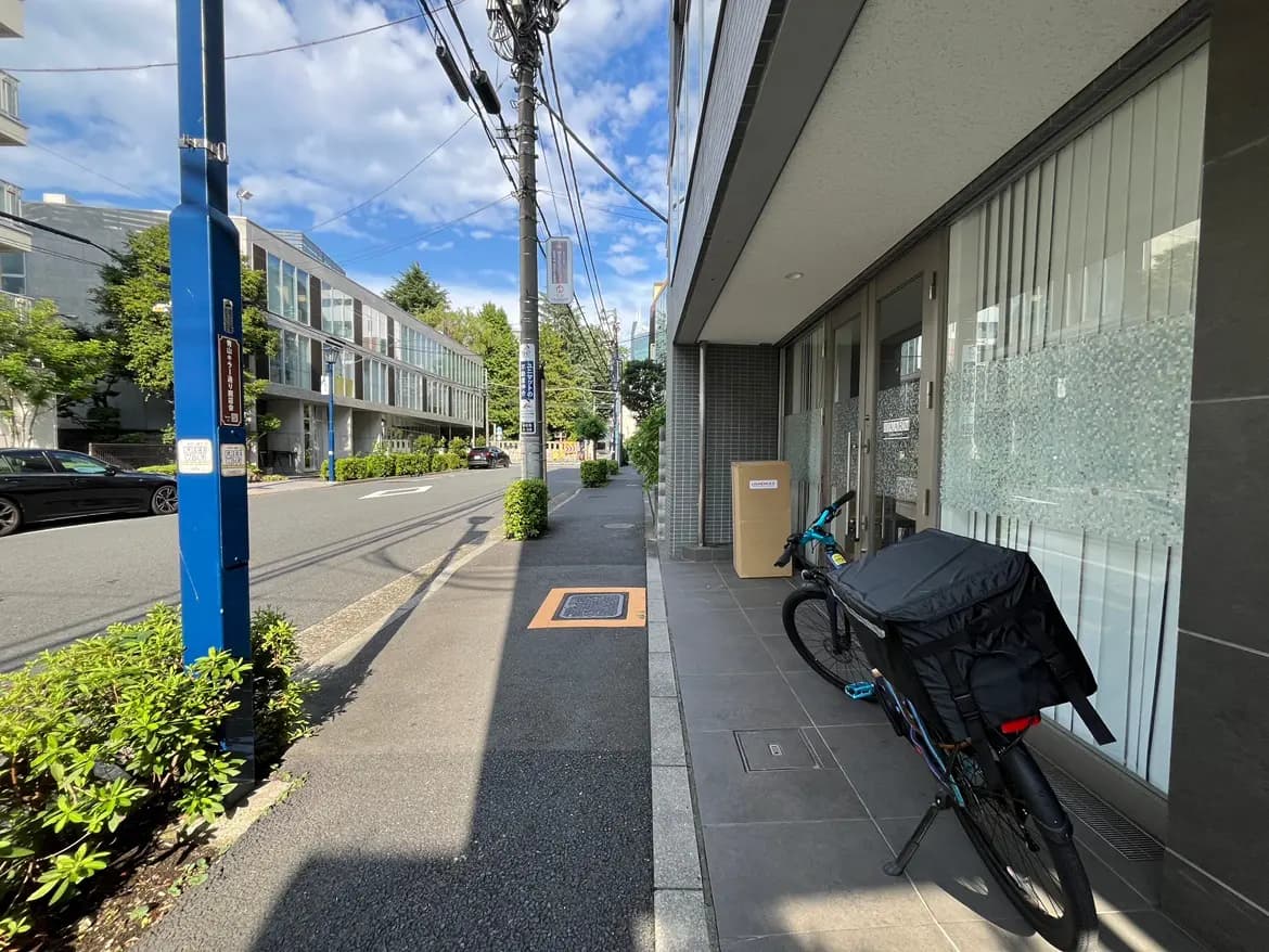 - 近代的な建物の前に停まっている自転車、整然とした歩道と街路樹、晴れた空が広がる都市の風景