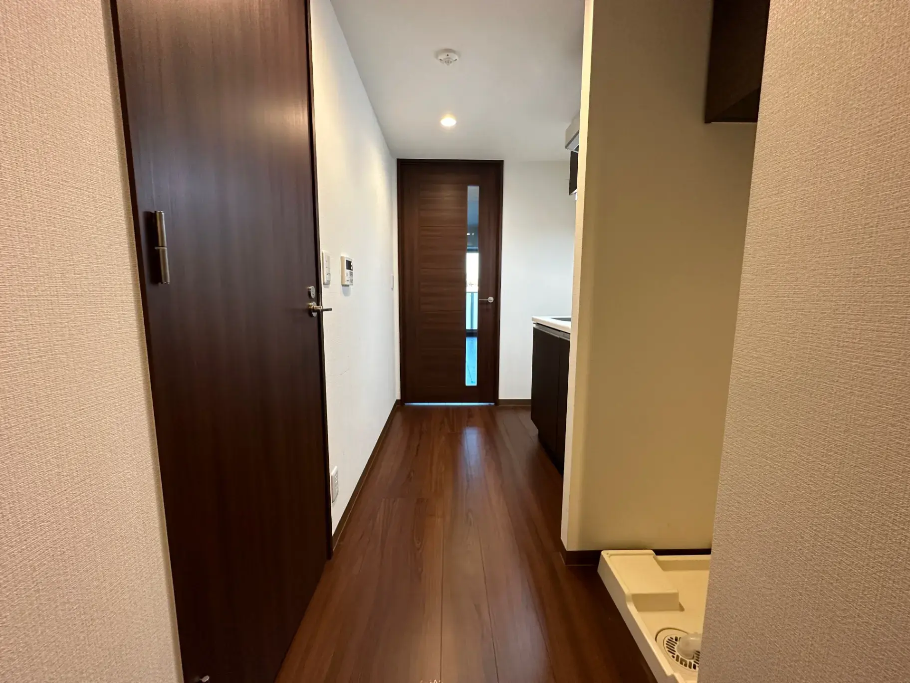 新築マンションの内廊下、木目調の床と白い壁、明るい照明と清潔感のある空間デザイン