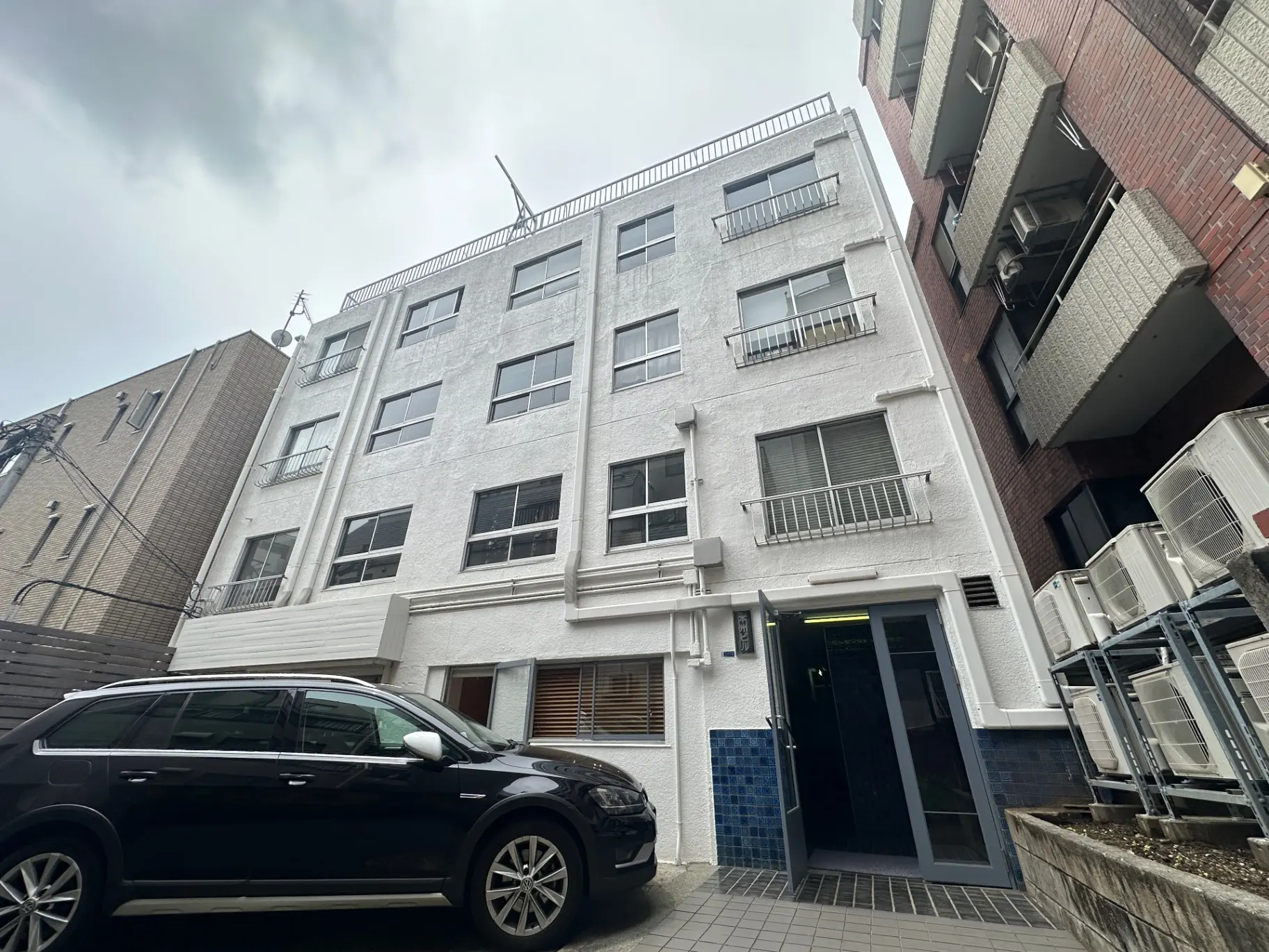 都市のアパートビルの外観、白い壁に窓が並ぶデザイン、周囲に他の建物が見える街並み