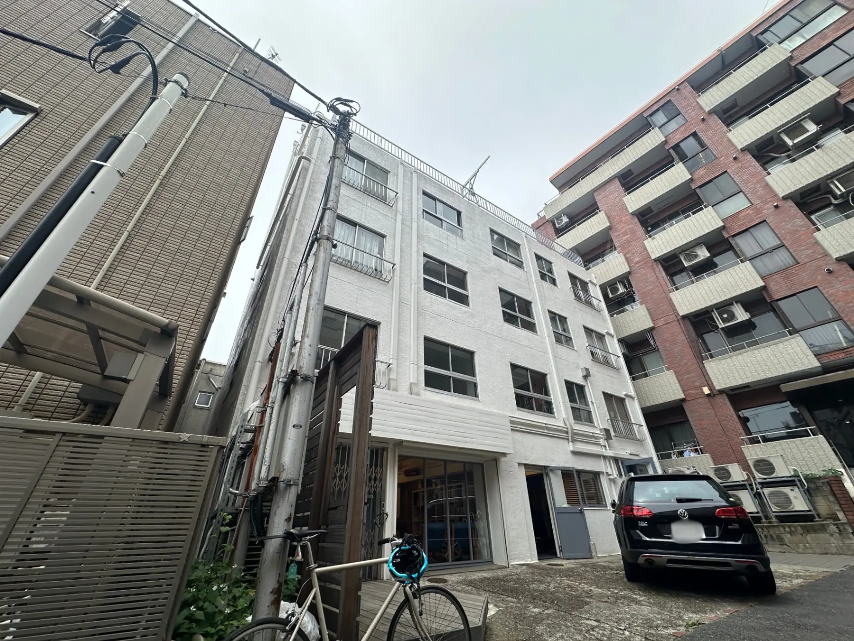 都市のアパート群、配管が見える外観、駐車中の車と自転車がある風景
