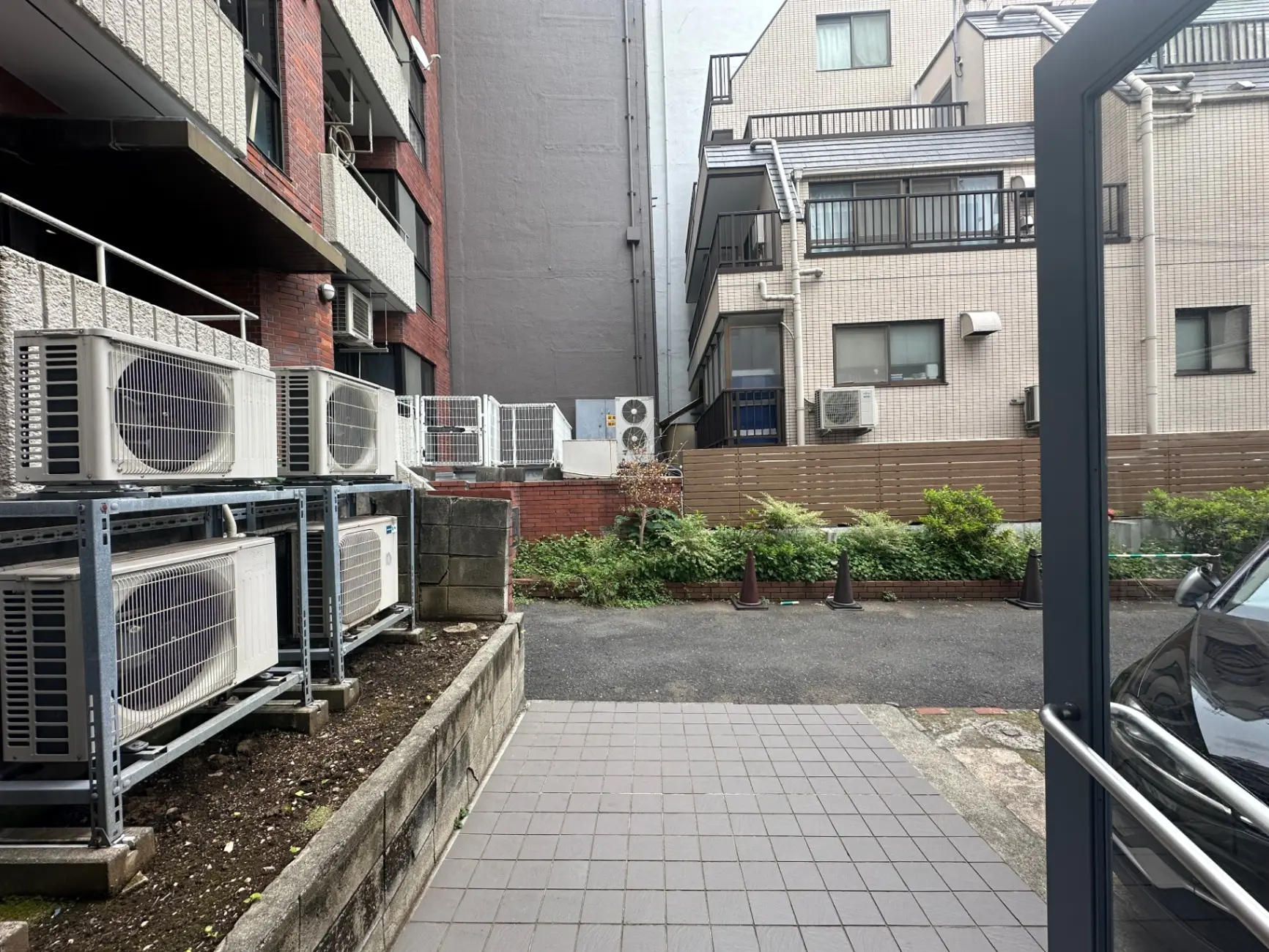 日本の住宅街の駐車場と建物のエアコン外部ユニット、緑化されたスペースが見える都市風景